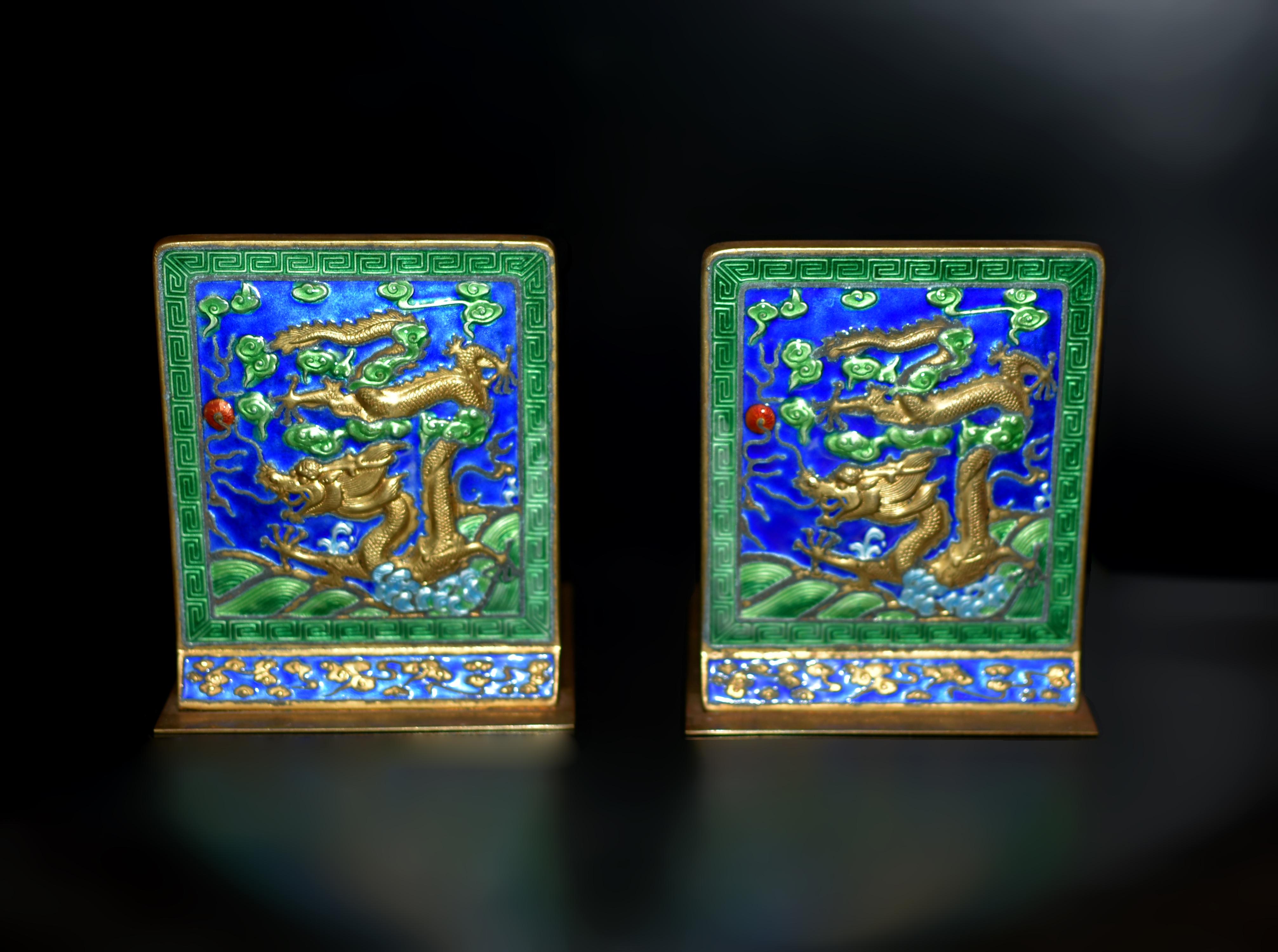 From a private collection, a spectacular pair of solid brass enameled bookends. Each features a gilded dragon emerging from ocean waves that meet the clouds, all five talons extended in pursuit of a fiery orb. The dragon's head strains forward in a
