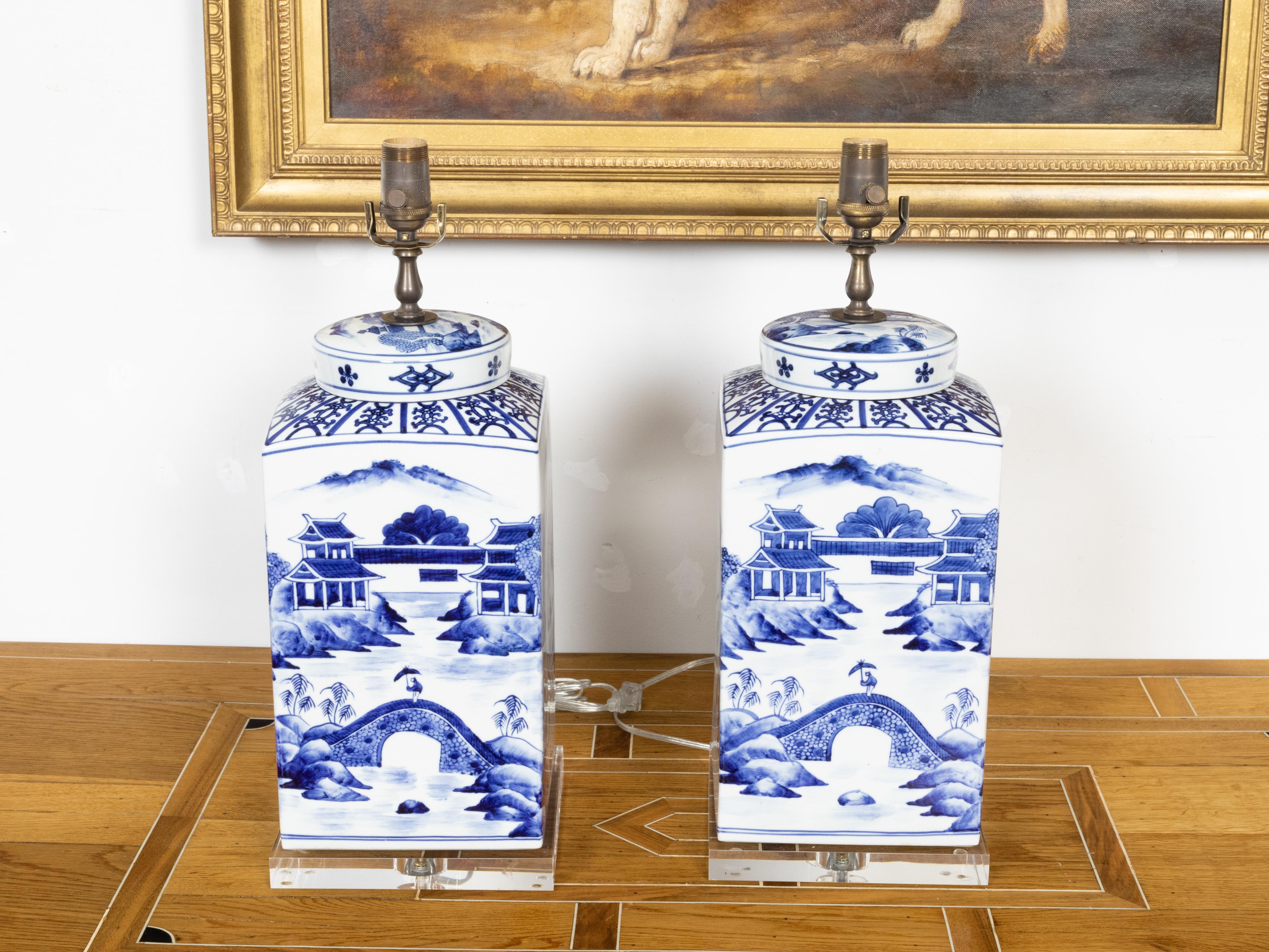A pair of Chinese Export blue and white porcelain jars with hand-painted Pagoda landscape scenes and newly mounted as table lamps on lucite bases. Created in China each of this pair of porcelain jars features a blue and white décor showcasing