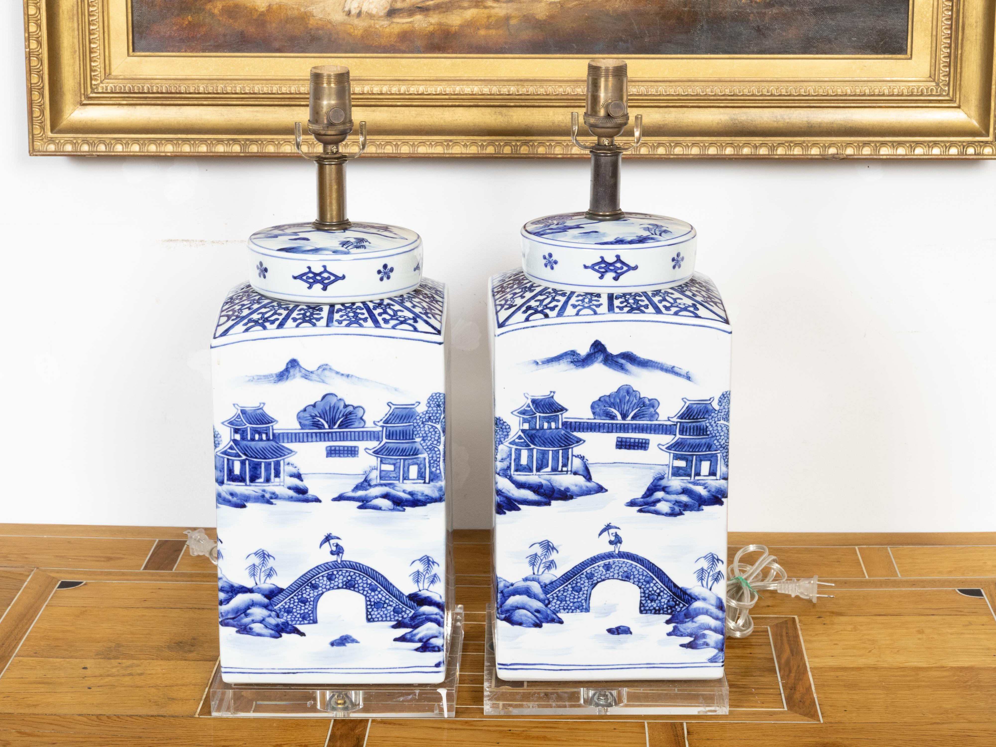 A pair of Chinese Export blue and white porcelain jars with hand-painted Pagoda landscape scenes and newly mounted as table lamps on lucite bases. Created in China each of this pair of porcelain jars features a blue and white décor showcasing