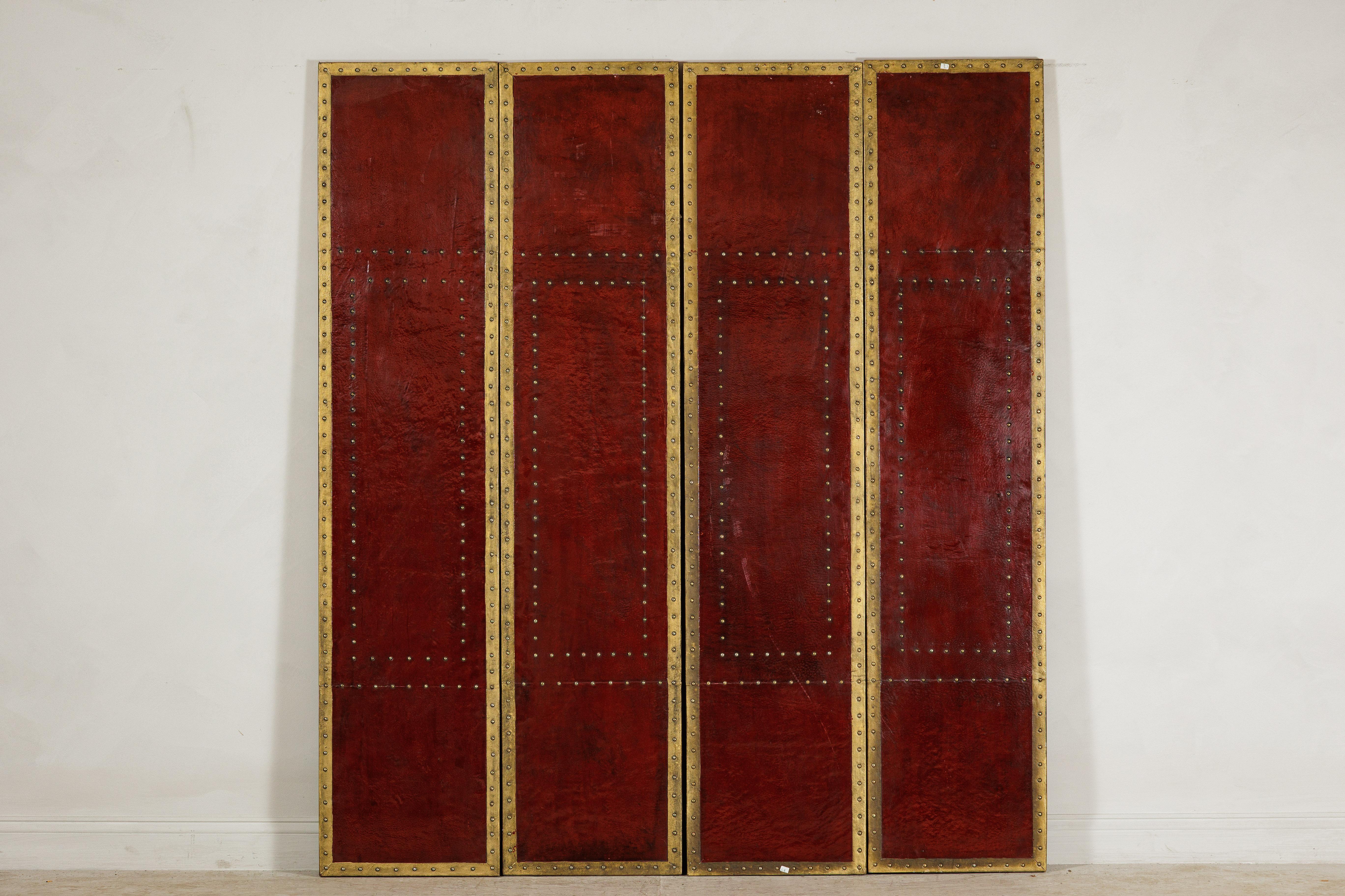 A vintage Chinese four-panel screen, crafted with bold oxblood-toned leather panels accented by brass nailhead trim. Each rectangular panel is edged with brass borders and punctuated by decorative nailheads that outline central and peripheral