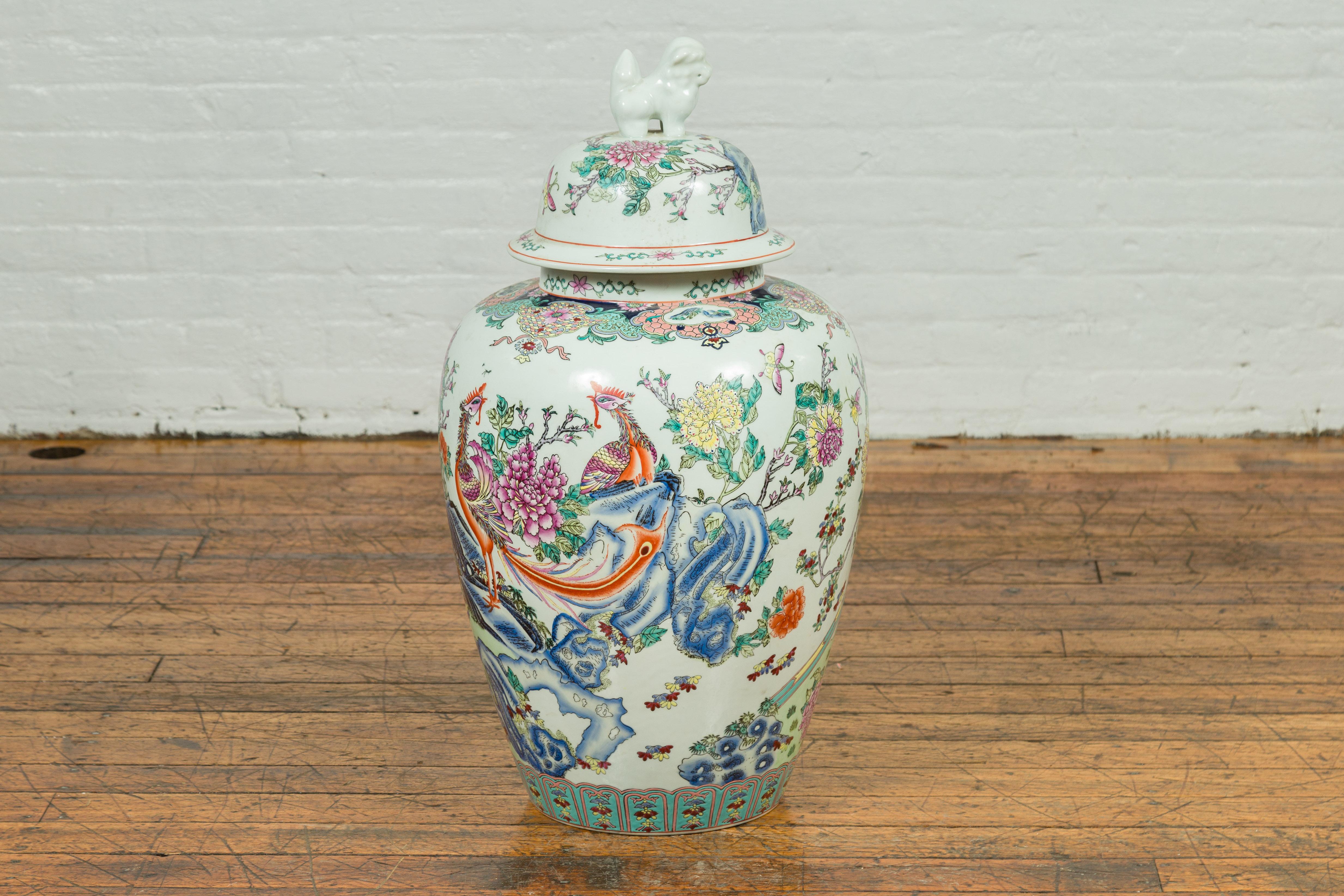 A vintage Chinese palace jar from the mid-20th century, handmade and painted on porcelain and topped with an animal figure. This tall jar features a phoenix among rocks and flowers. This flower and bird theme is common in Chinese painting, but the