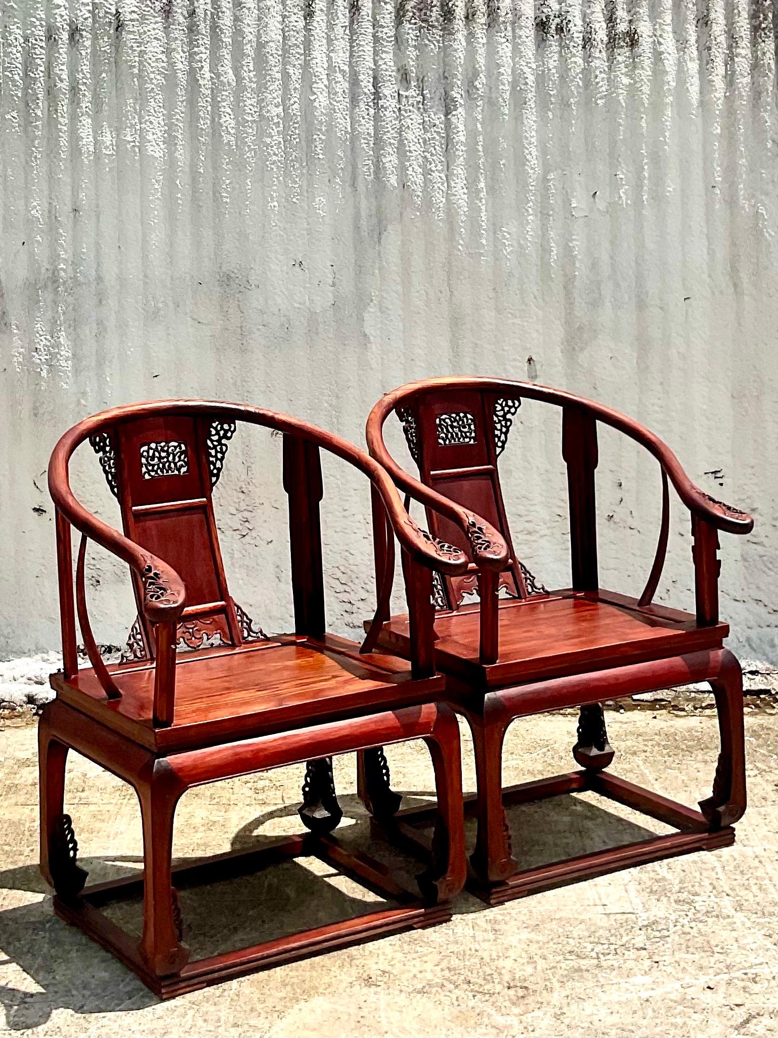 Stunning pair of 20th century Huanghuali style arm chairs. Each have intricately carved backsplats with curvilinear arms that end in a scrolled flourish. Acquired from a Palm Beach estate.