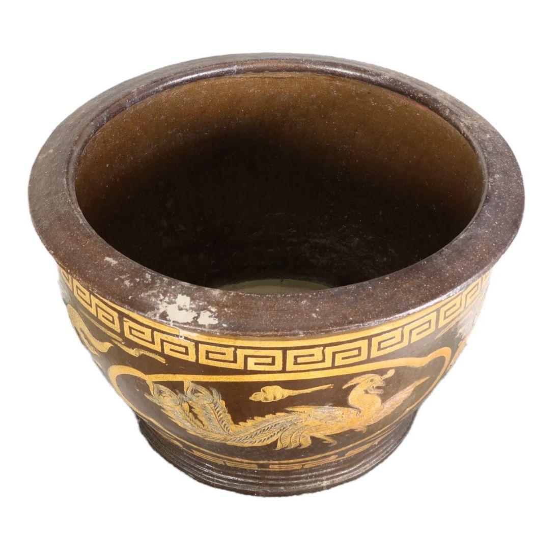 Questo vaso in terracotta di ispirazione cinese Vintage presenta una ricca finitura marrone ornata da intricati motivi decorativi dorati, tra cui fenici e motivi stilizzati che ricordano i disegni tradizionali cinesi. La forma arrotondata del vaso e