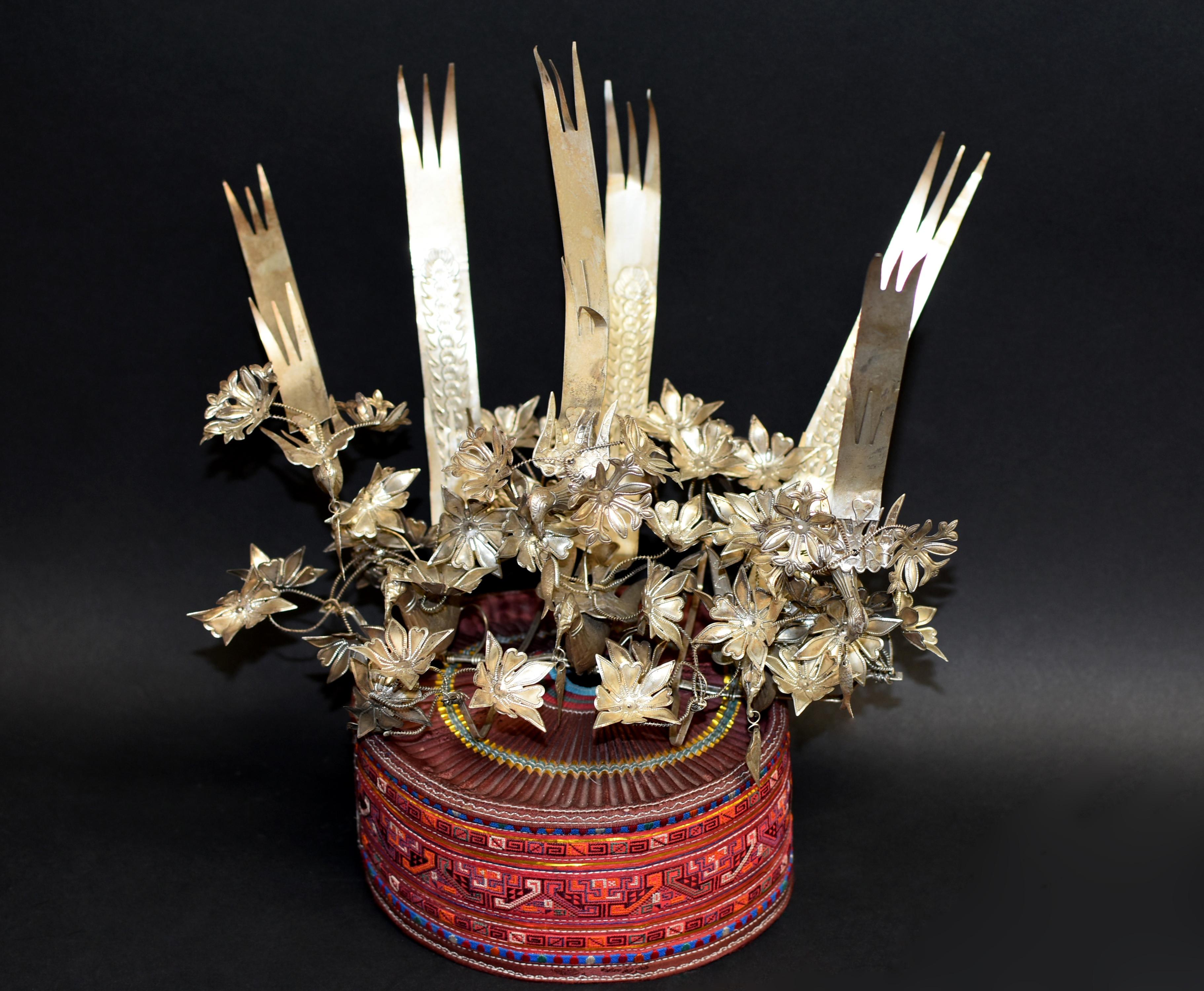 A beautiful hand made Miao tribe hat with silvered metal ornaments. The hand made hat is covered with embroidered bands. The prominent crown is decorated with 6 hand made phoenixes, among which three holding dangling fish in their mouths. The birds