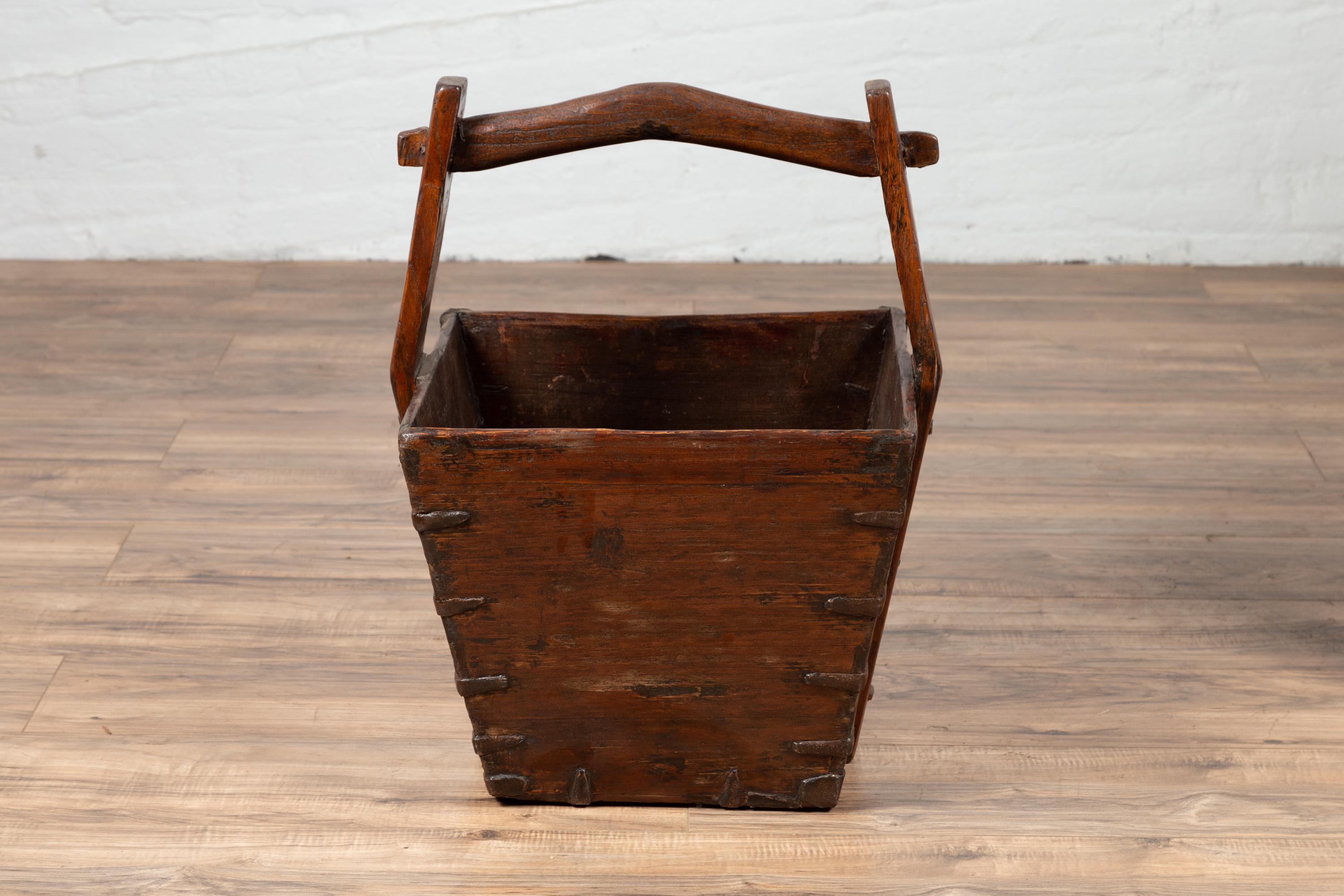 A Chinese vintage wood carrying box from the mid-20th century, with large handle and metal braces. Born in China during the mid-century period, this charming wood carrying box features a nicely tapered body, accented with metal braces in the corners