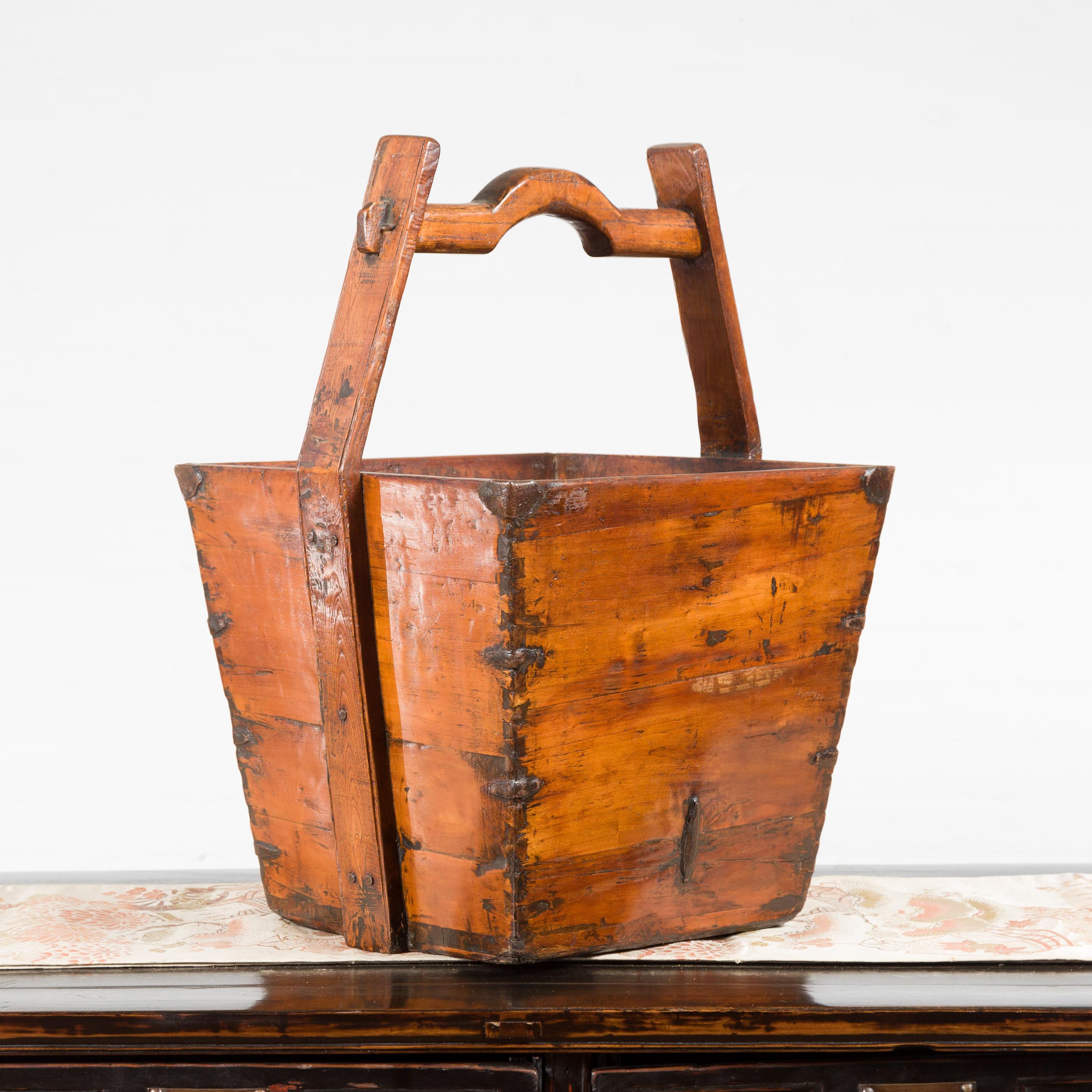 A Chinese vintage wooden grain basket from the mid-20th century, with large handle and metal braces. Created in China during the mid-century period, this grain basket features a nicely tapered body, accented with metal braces in the corners and
