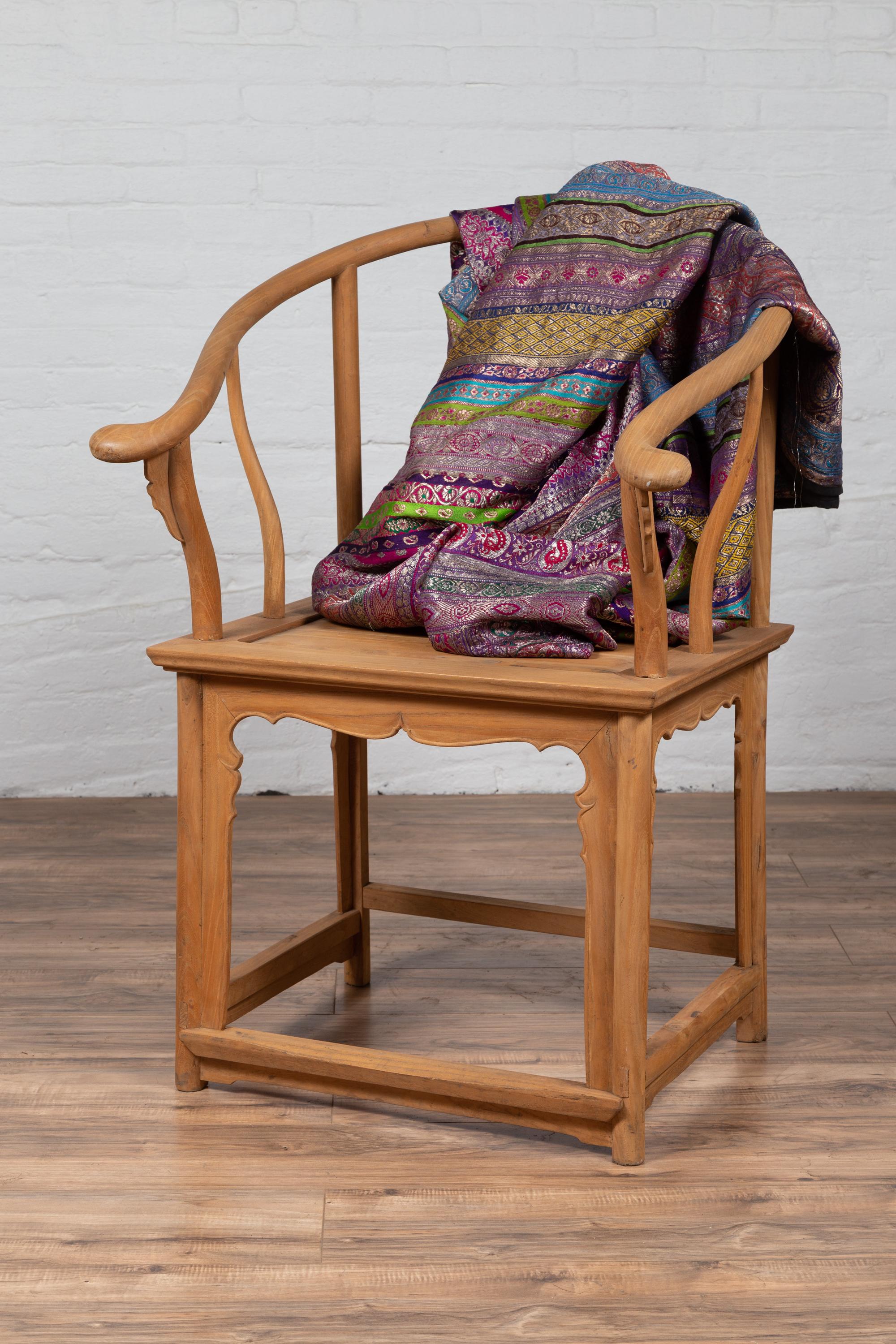 A Chinese vintage Ming dynasty style natural wood horseshoe back armchair from the mid 20th century, with carved splat and apron. Born in China during the mid-century period, this armchair charms our eyes with its natural wooden finish and graceful