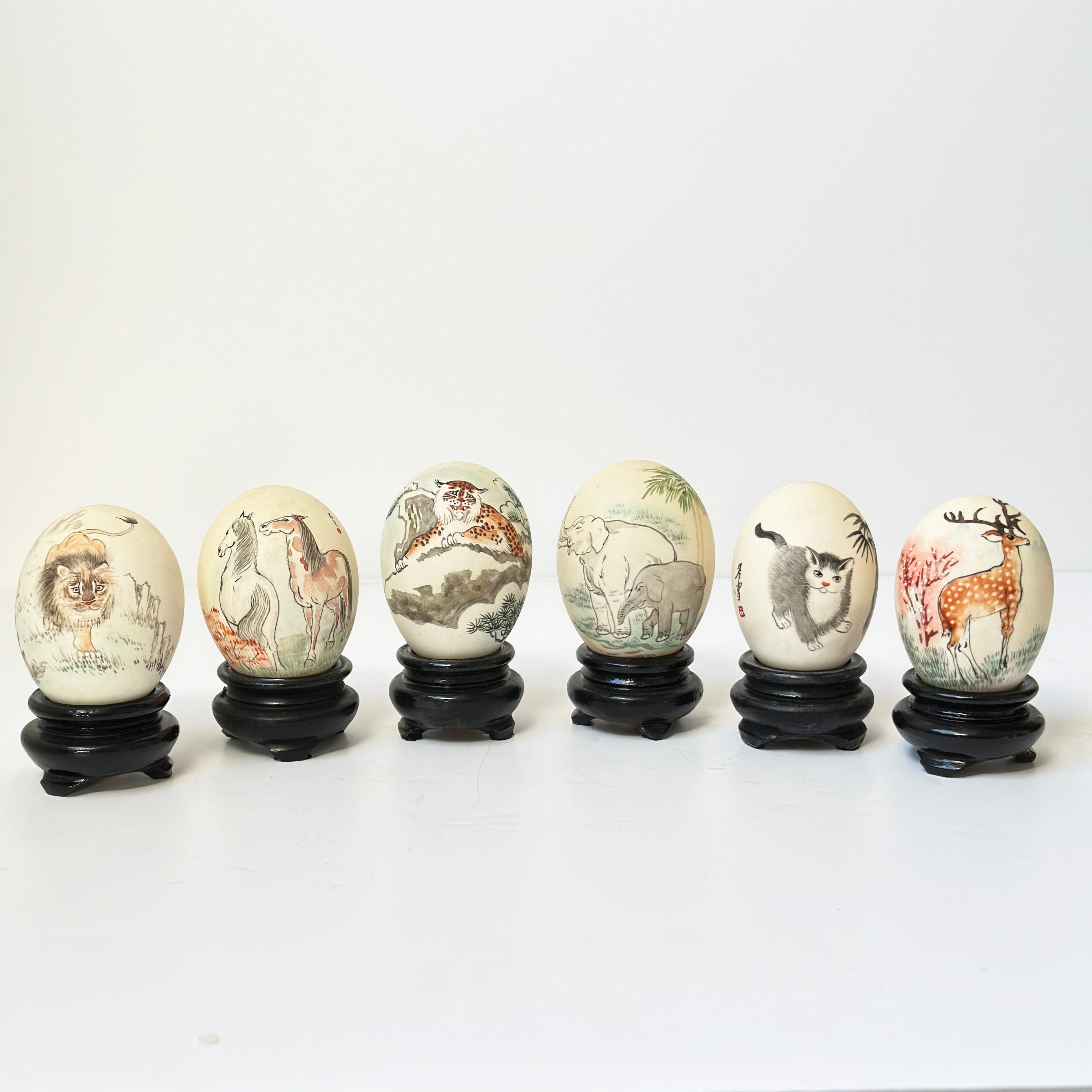 Œufs peints chinois vintage : cette collection présente une sélection de coquilles d'œufs peintes à la main, chacune étant mise en valeur sur un socle en bois sculpté. Ces pièces ont été fabriquées par des artistes spécialisés dans les coquilles