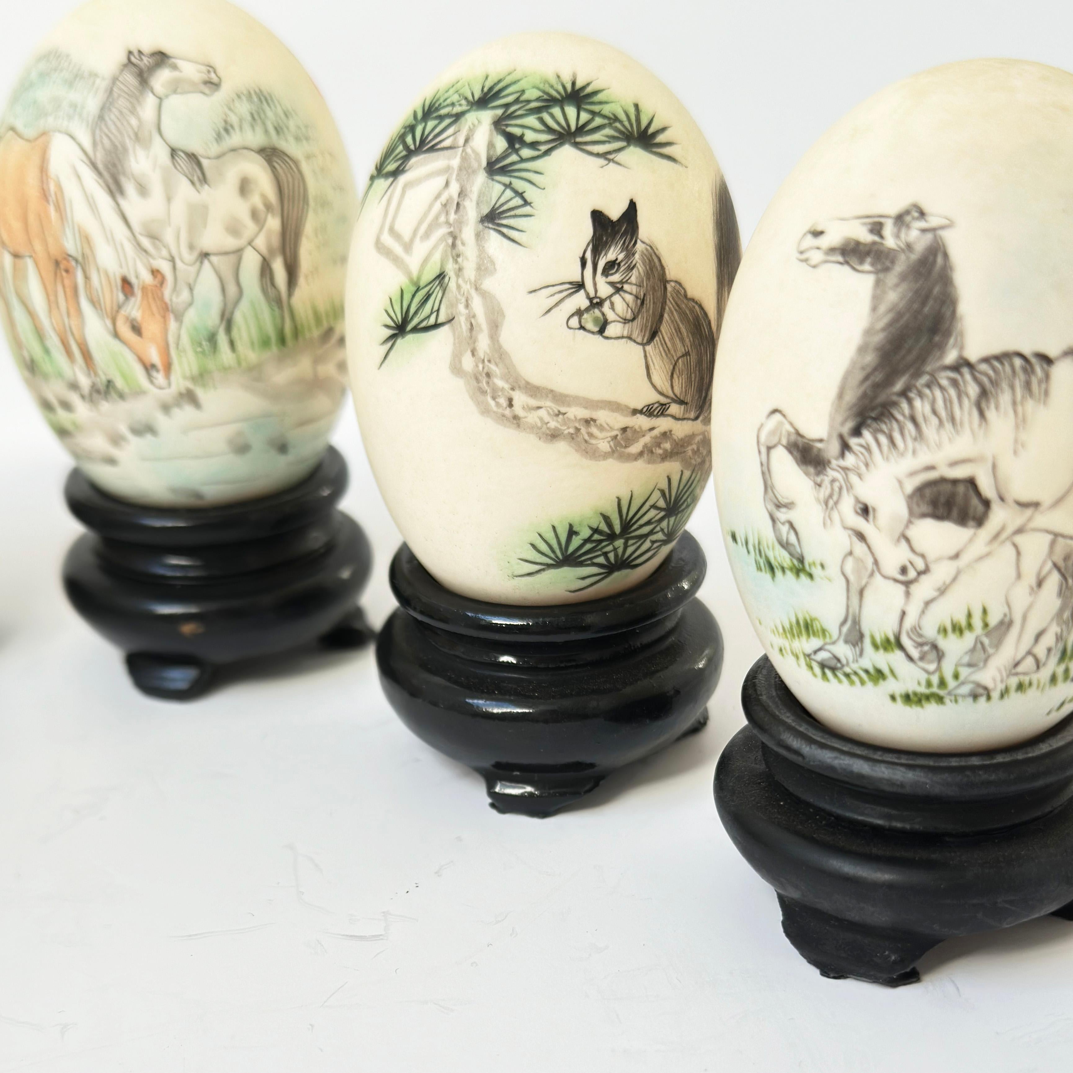 Vintage Chinese Painted Eggs: This collection features a selection of hand-painted eggshells, each showcased on a carved wooden plinth. These pieces were crafted by skilled eggshell artists in China during the 1970s. The intricately applied