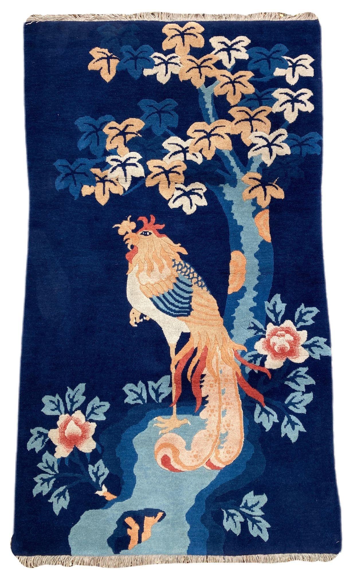 Un joli tapis Pao-Tao vintage, tissé à la main en Chine vers 1940. Le motif représente un seul oiseau Fenghuang devant un arbre en fleurs sur un champ indigo profond. Cet oiseau mythique est un symbole de bon augure représentant la haute vertu et la