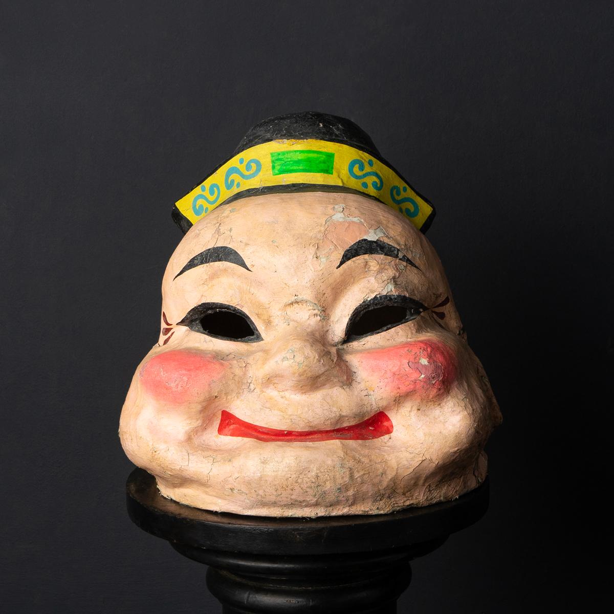 Mid-century theatre/festival mask.
An extremely characterful mask depicting a chubby face with bulbous, rosy cheeks and a big grin.

Made from paper mache with wirework and wood underneath and then hand painted in vibrant colours.

Originally