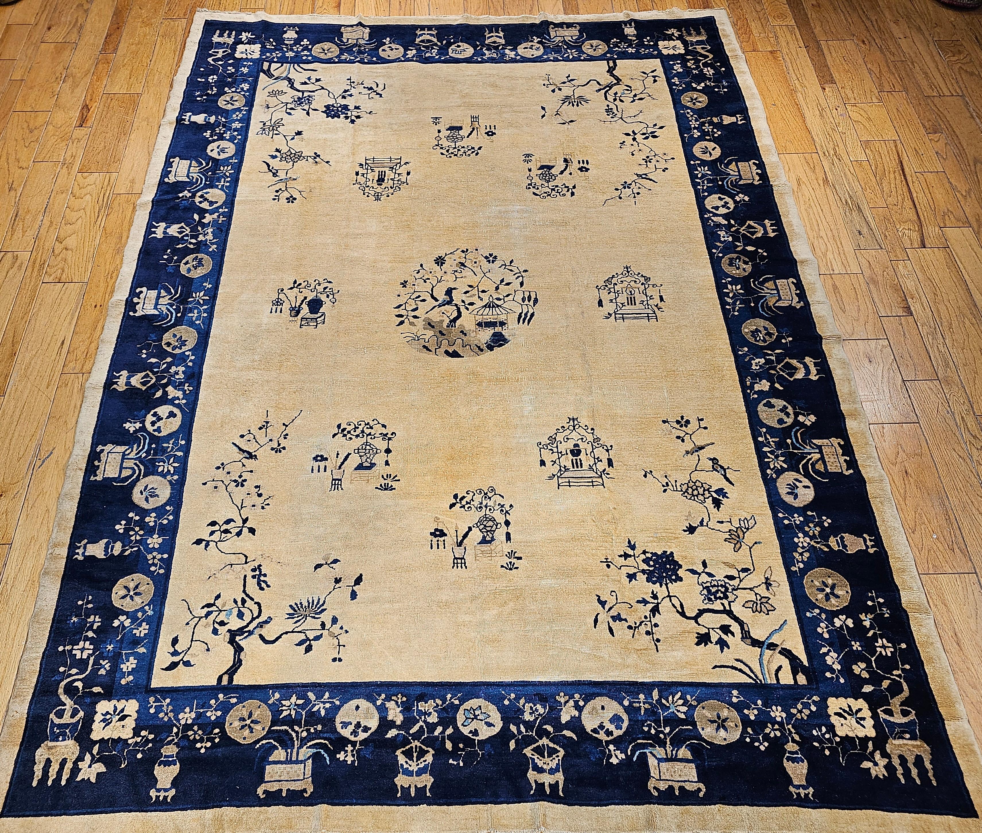 Vintage Chinese Peking room size rug from the late 1800s,  The rug has a pale yellow or tan main field color and a navy and French  blue color on the border. The design of the trees, branches, planters, and birds in the corners and throughout the