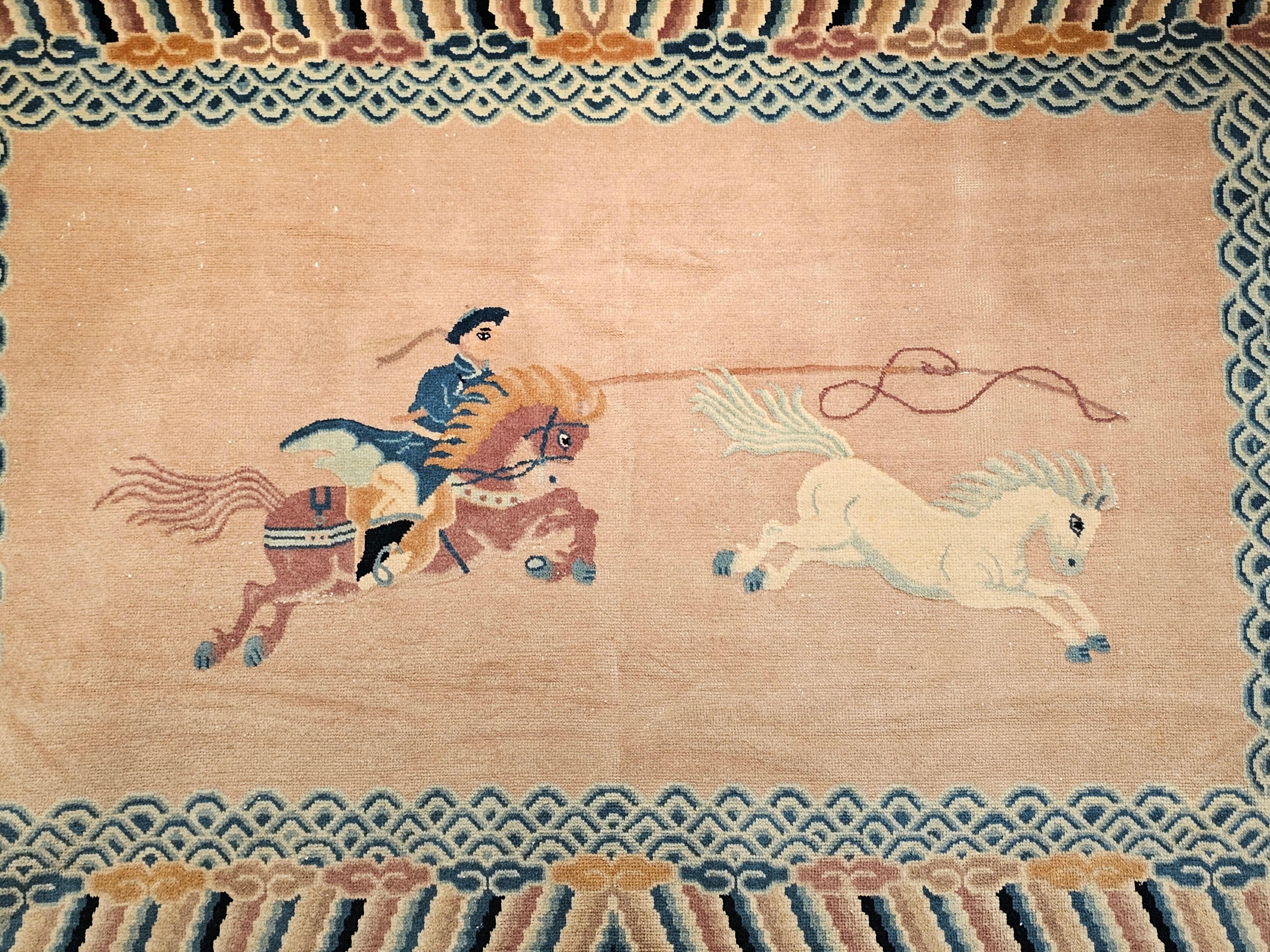 Vintage Chinese pictorial rug depicting a man on the back of the horse throwing a rope loop to capture a running wild horse.  The design is set on a pale pink background with multi-color border similar to the rugs from Khotan.   The rug has a wool