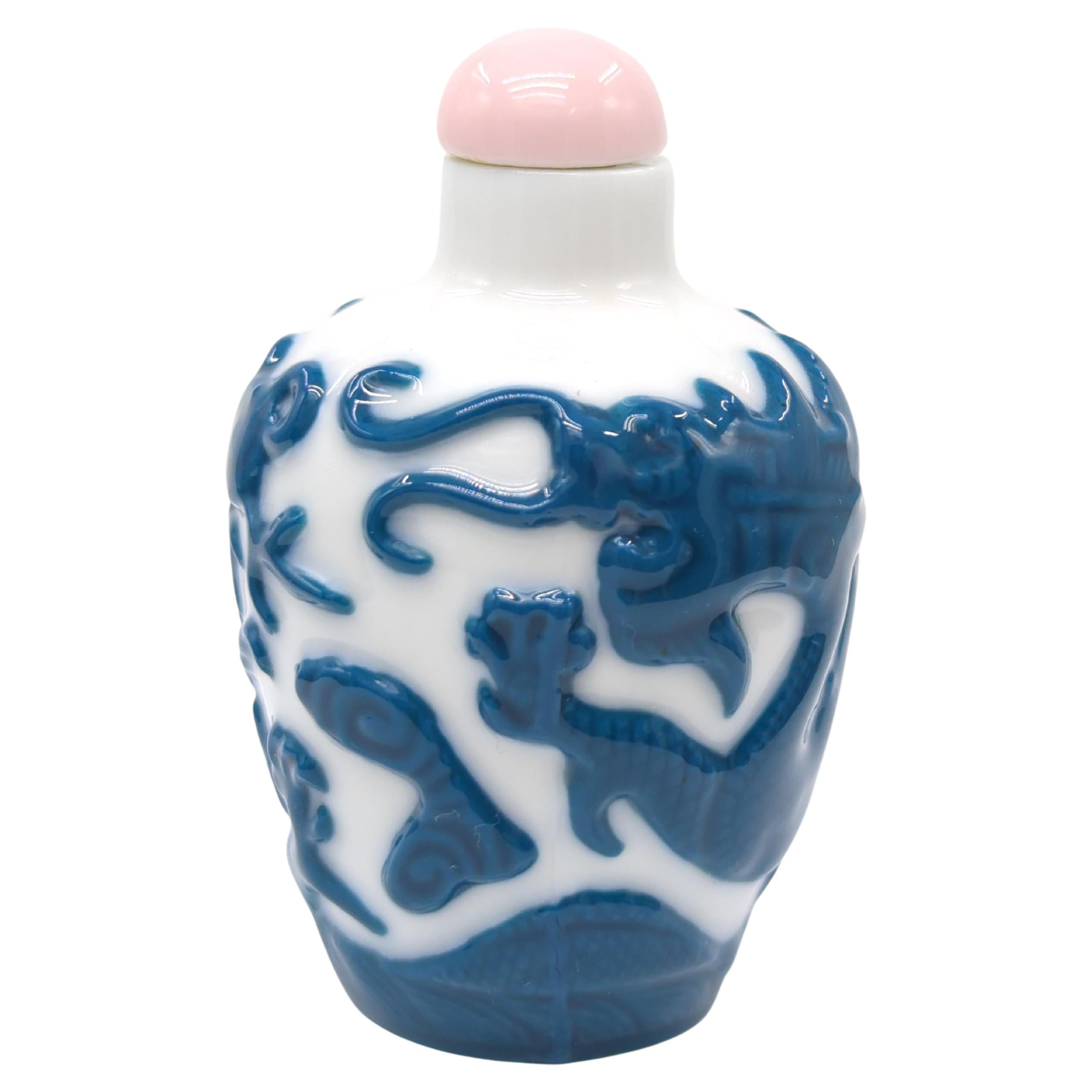 A vintage Chinese porcelain snuff bottle, finely decorated with two scaly slithering cobalt blue five claw dragons contesting a flaming pearl, carved in relief above a border of crashing waves

circa: mid 20th Century