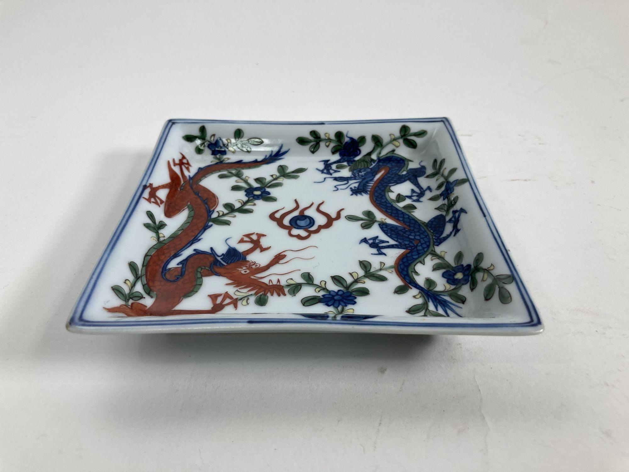 Vintage Asian square porcelain dish, ashtray or catchall.
Chinese Wanli Wucai style porcelain square dish with dragons and floral decoration. 
Asian themed white square porcelain hand painted with a blue dragon and one red dragon chasing a fire