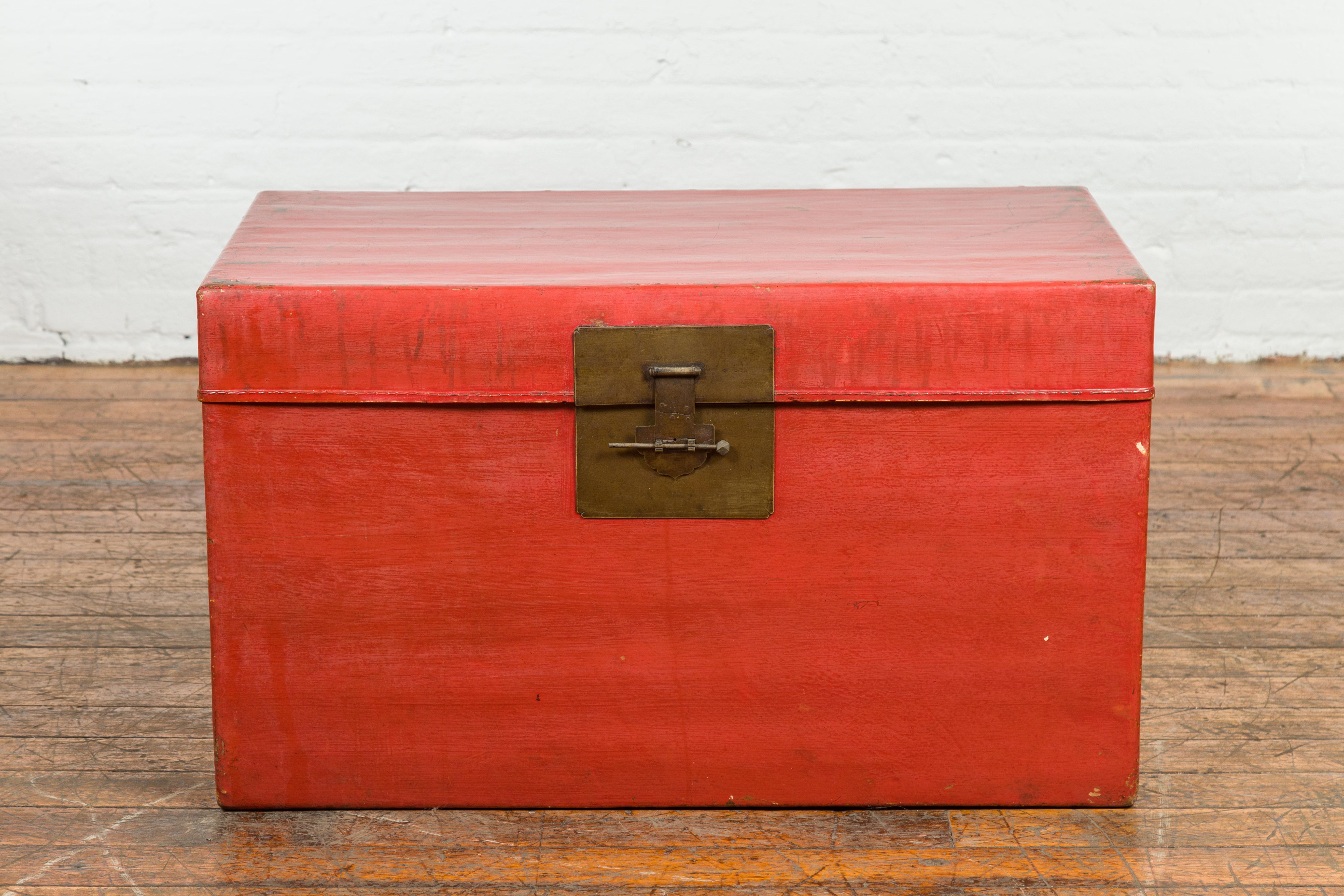 A vintage Chinese red lacquer blanket chest from the mid 20th century with brass hardware and lateral c-scroll handles. This mid-20th-century Chinese red lacquer blanket chest manifests an exquisite blend of simplicity, functionality, and