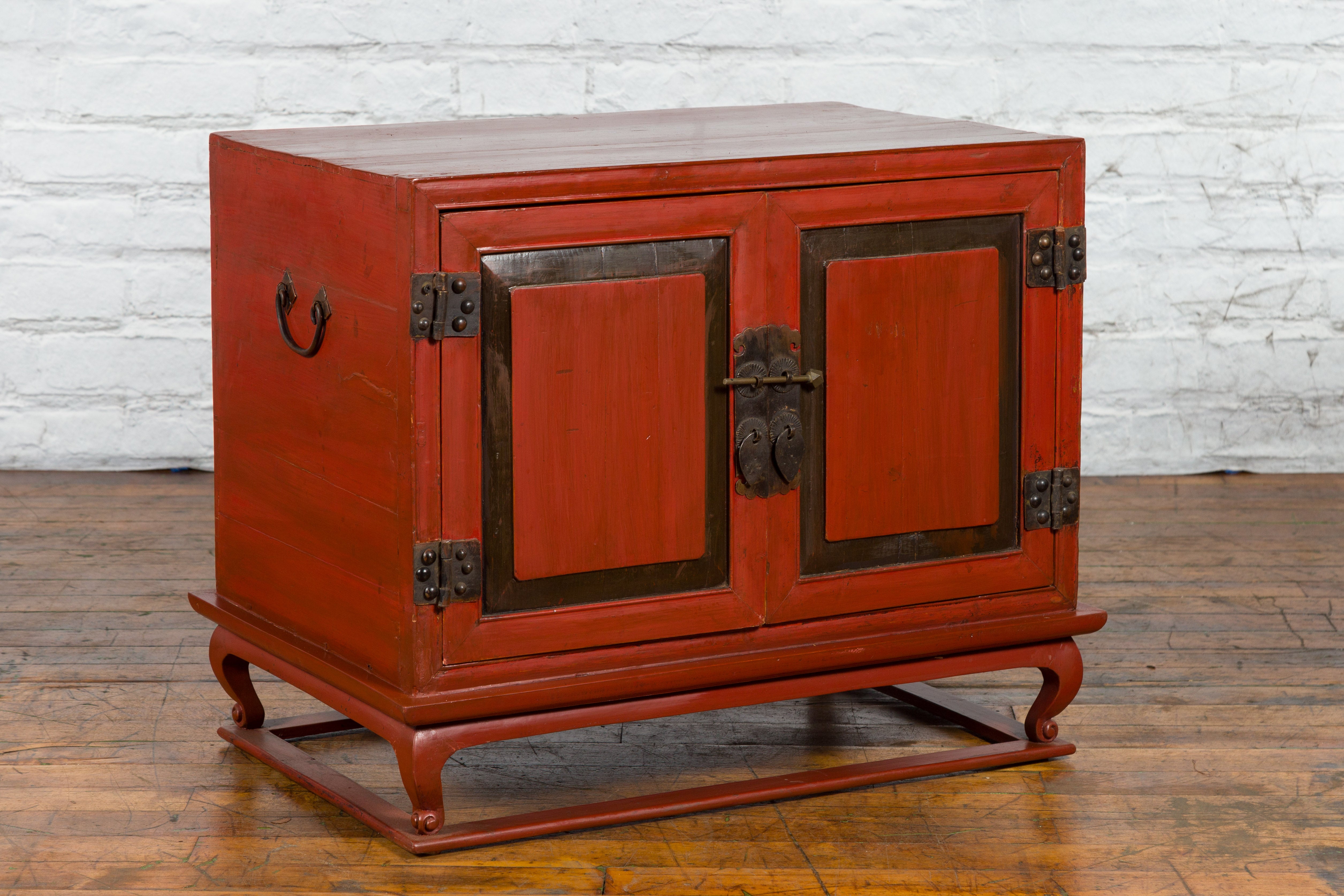 A vintage Chinese small cabinet from the mid 20th century with red lacquer, cabriole feet and brass hardware. Created in China during the Midcentury period, this small cabinet showcases a red lacquered finish complimenting the clean lines