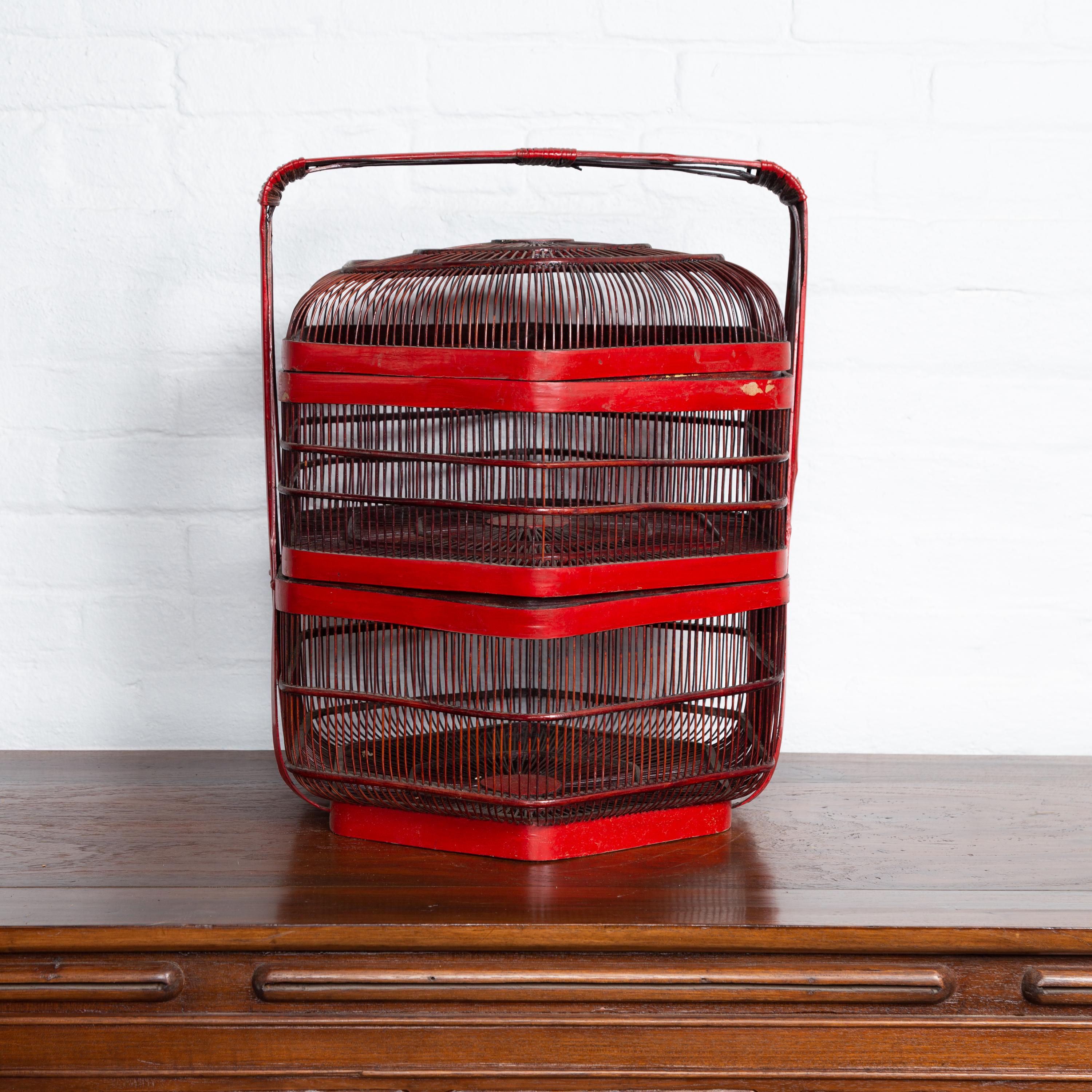 A Chinese vintage red lacquered bird cage from the 20th century with handle and hexagonal base. Born in China during the second quarter of the 20th century, this charming bird cage features a red lacquered surface, accented with delicate cartouches