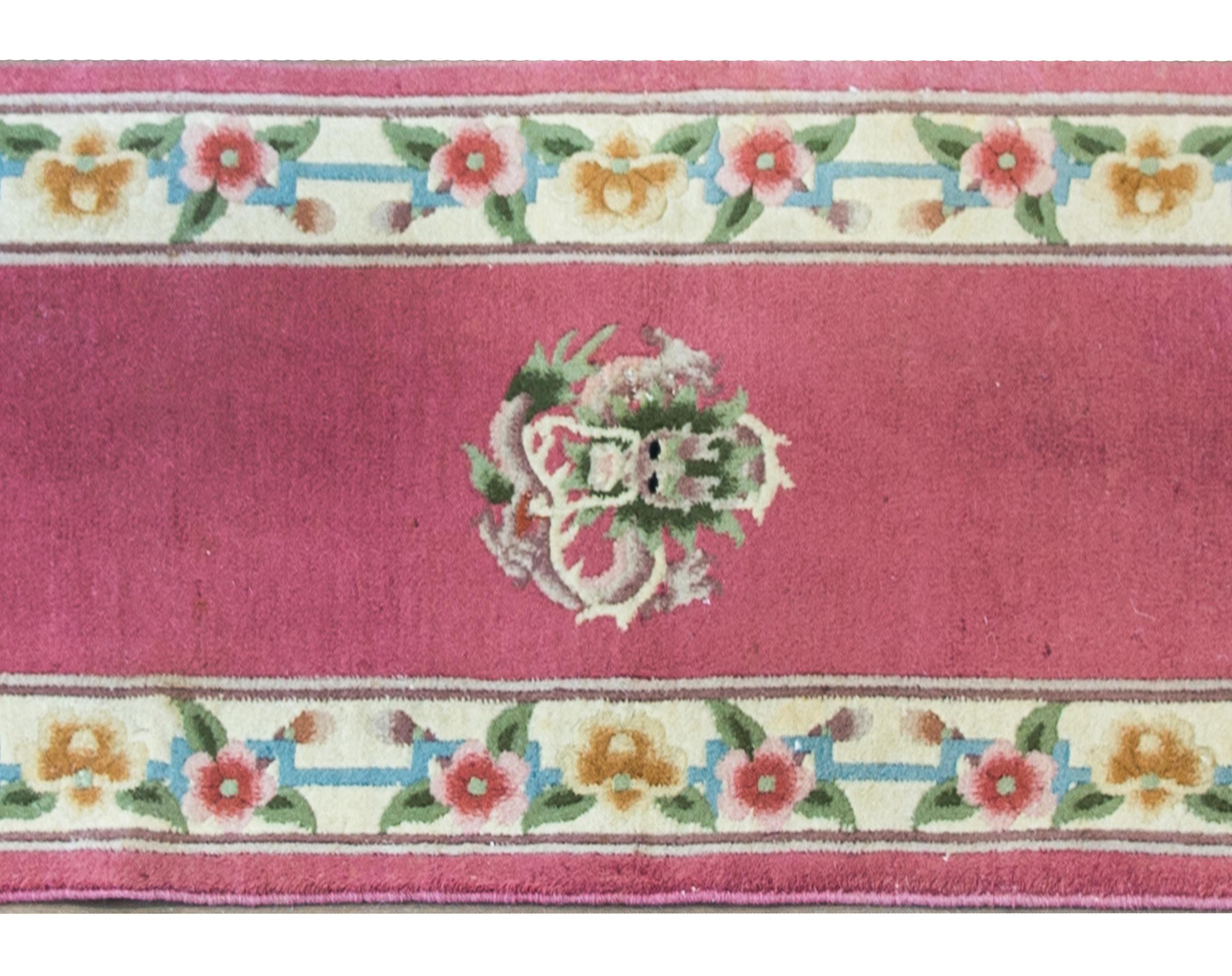 A wonderful mid-20th century Chinese runner with a pale fuchsia field with a central swirling dragon medallion flanked by pairs of peony and lotus medallions, and completely surrounded by more stylized peonies.