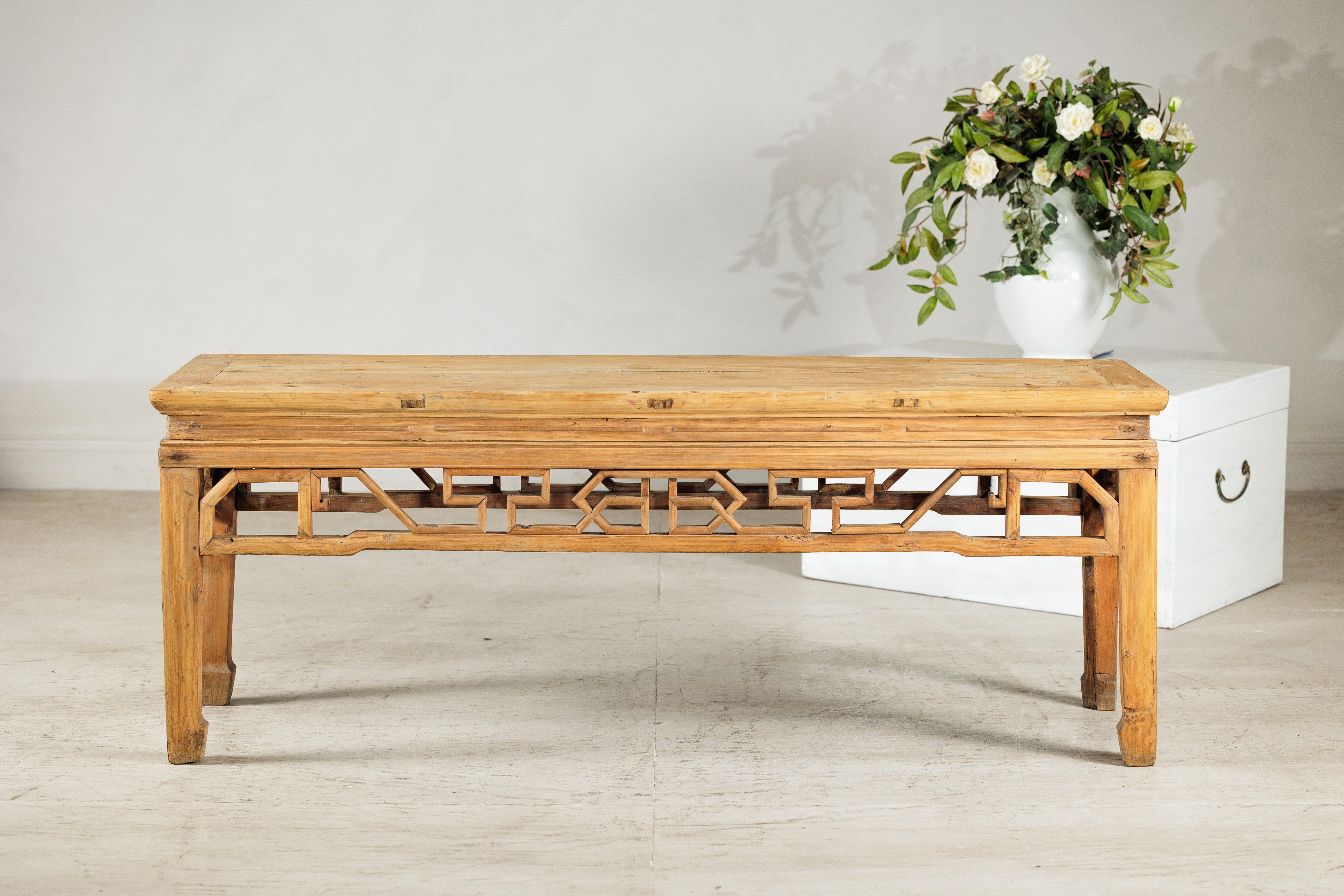 This vintage Chinese low table combines rustic simplicity with the refinement of traditional craftsmanship. The rectangular top, made from naturally aged wood, sits over an intricately carved apron, where geometric openwork patterns lend rhythm and