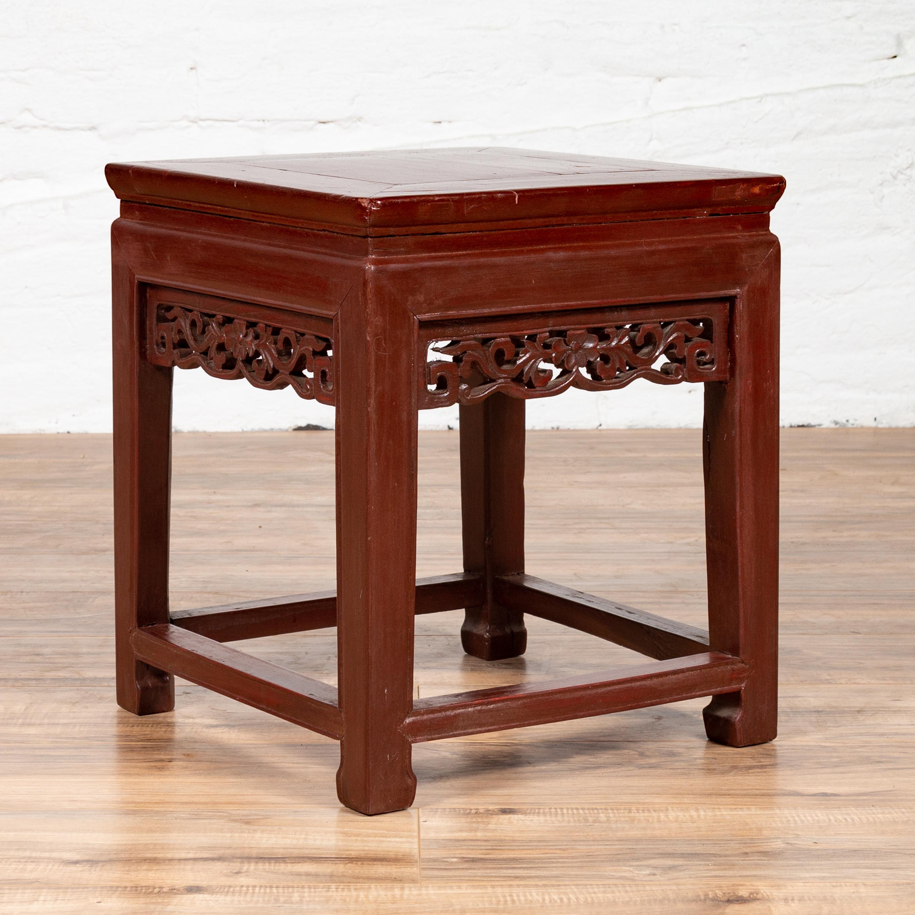 A Chinese vintage waisted side table from the mid 20th century, with dark red wooden patina and carved apron. This Chinese side table presents a perfect contrast between the gentle linearity of its silhouette, and the delicate curves of its carved