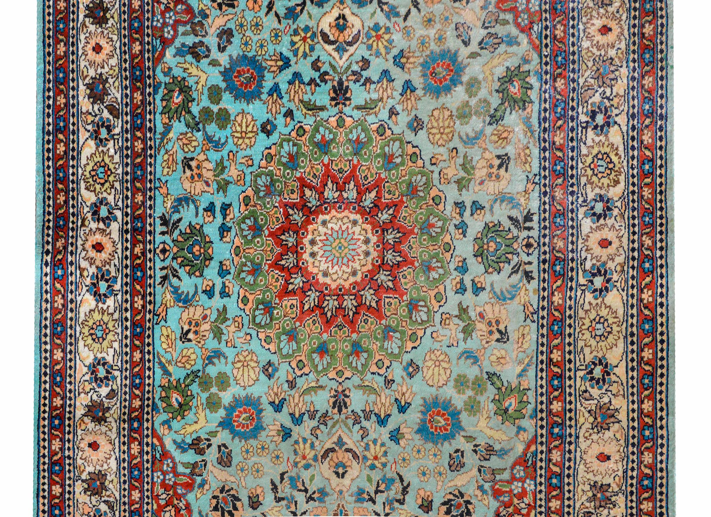 A beautiful vintage Chinese silk rug with a large central floral medallion amidst a field of large-scale flowers all woven in light and dark indigo, cream, green, and white against a light sky blue background, and surrounded by a wide floral