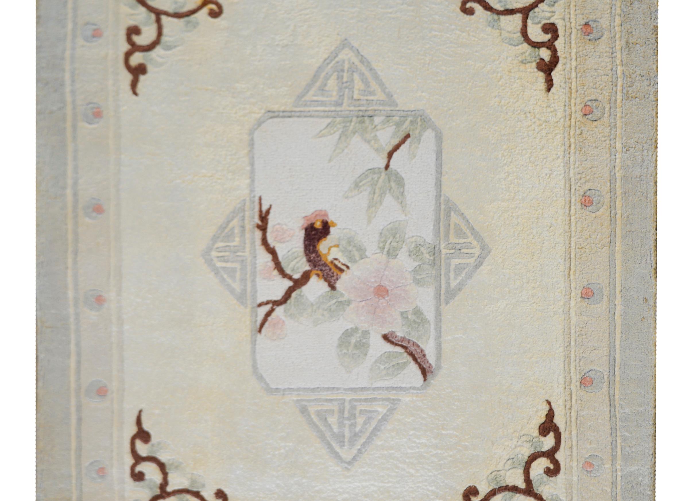 A simple but beautiful hand woven Chinese silk rug depicting a central medallion of a phoenix resting on the branch of cherry tree with a blossom on the foreground. The medallion is surrounded by more cherry blossoms against a cream colors
