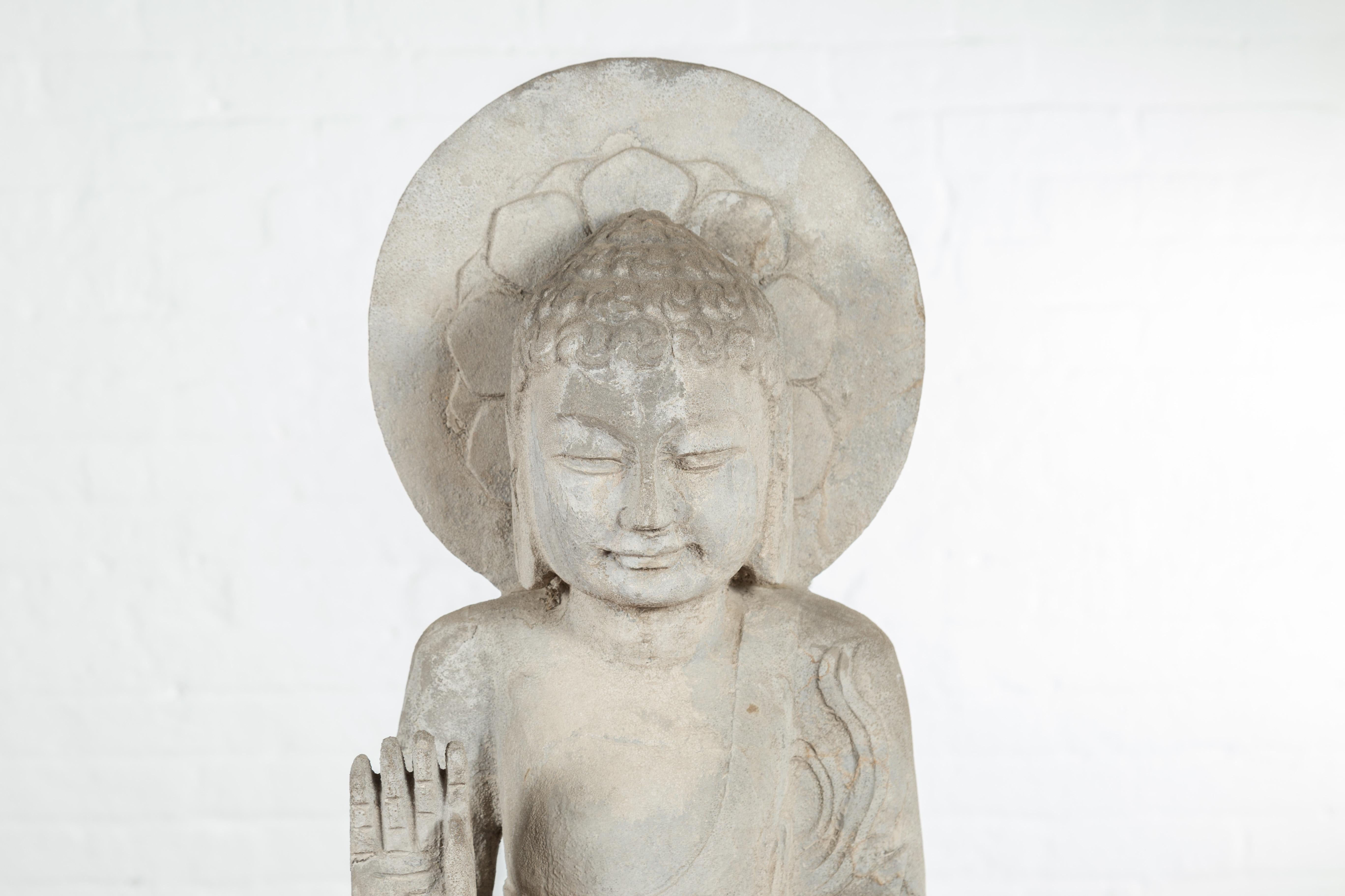 A vintage Chinese carved stone standing Buddha with Abhayamudra from the mid-20th century. Created in China during the midcentury period, this standing Buddha features the Abhaya mudra, the gesture of fearlessness. This mudra represents protection,