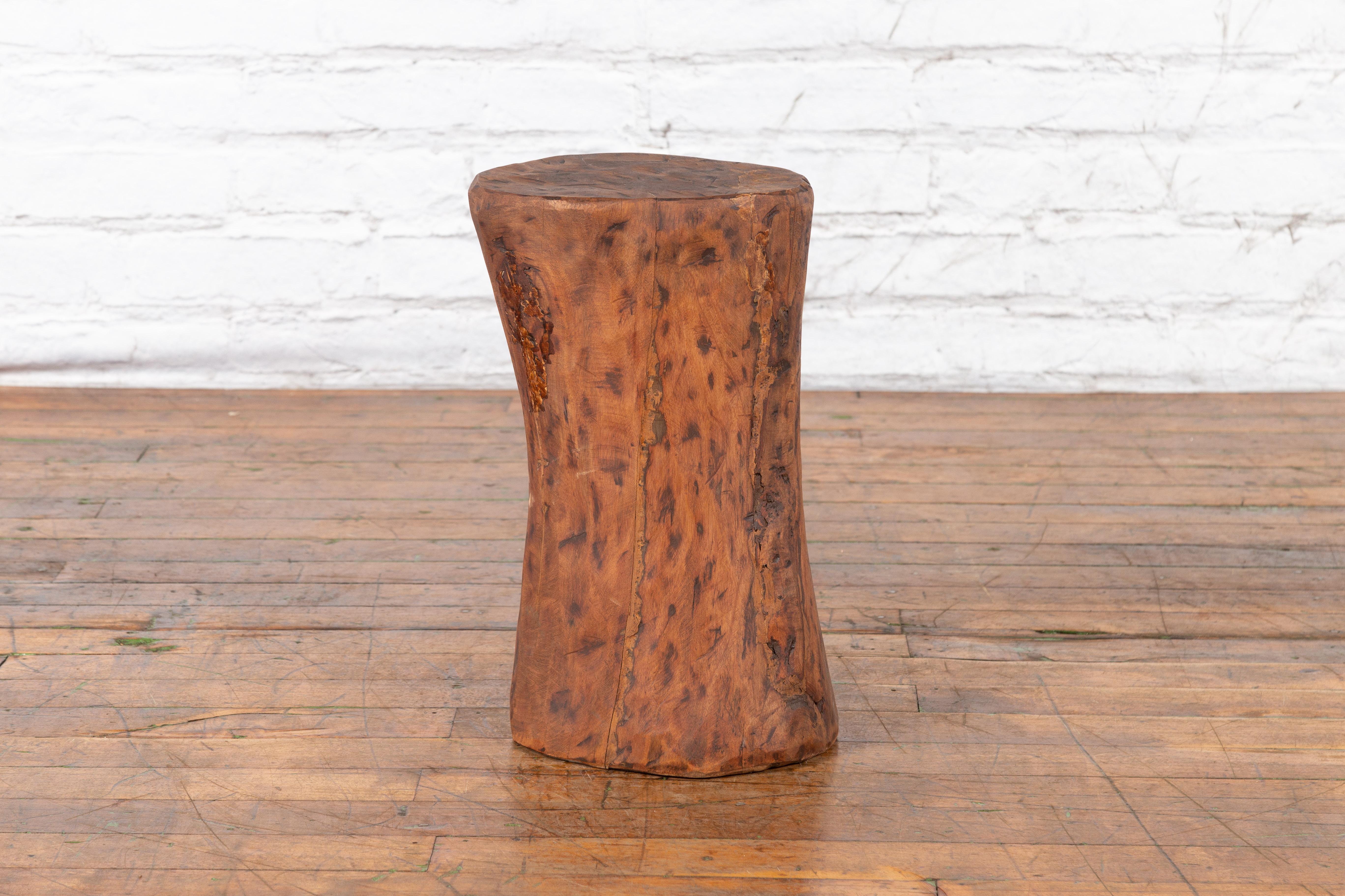 A vintage rustic Chinese wooden tree stump pedestal from the mid 20th century with distressed patina. Created in China during the Midcentury period, this wooden pedestal charms us with its nice rustic appearance and brown textured body. Flat at the