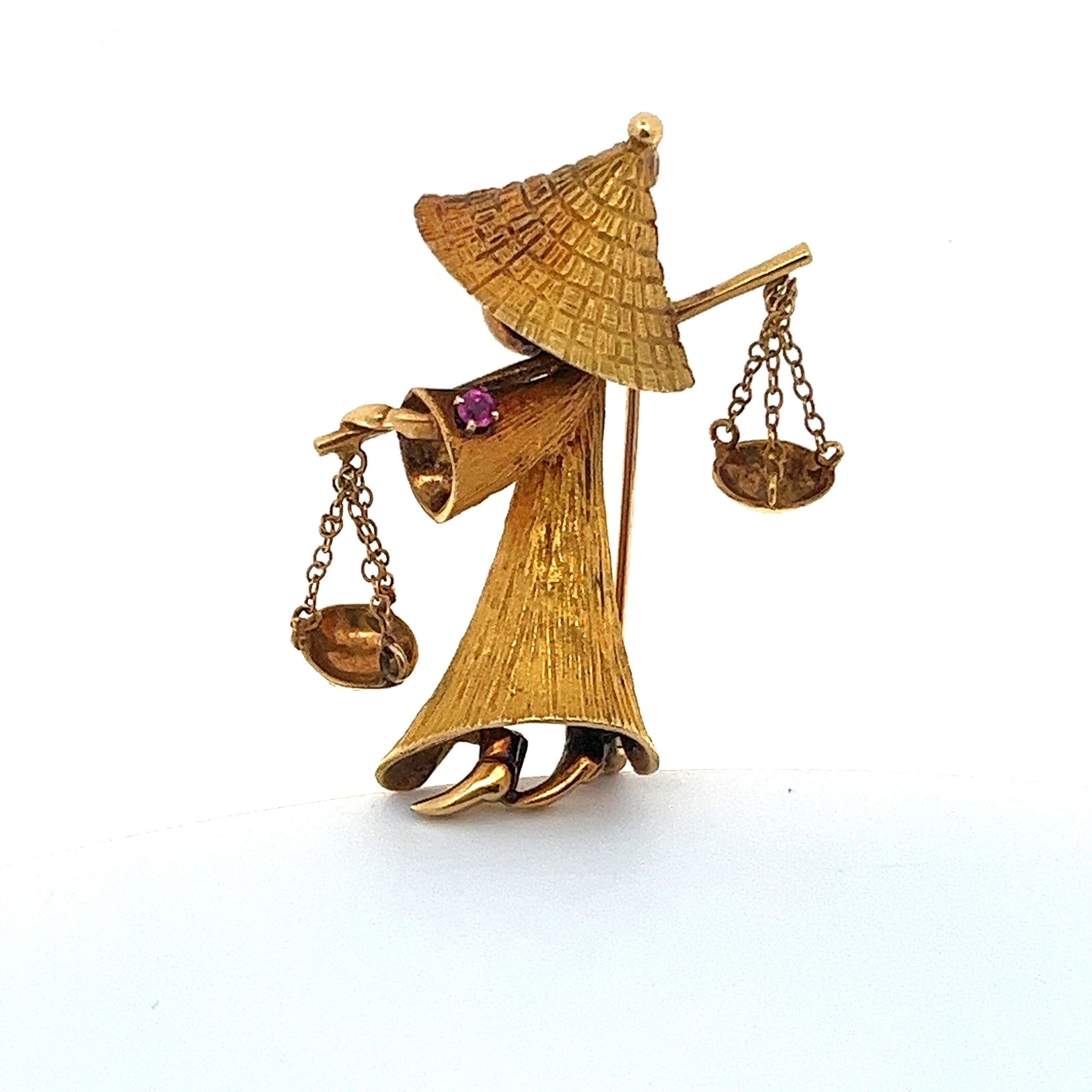 This meticulously handcrafted pin showcases a water carrier boy, crafted from 18 karat yellow gold. The figure is depicted wearing a traditional Asian conical hat and carrying two delicately moving buckets. A subtle highlight is the .05 carat ruby