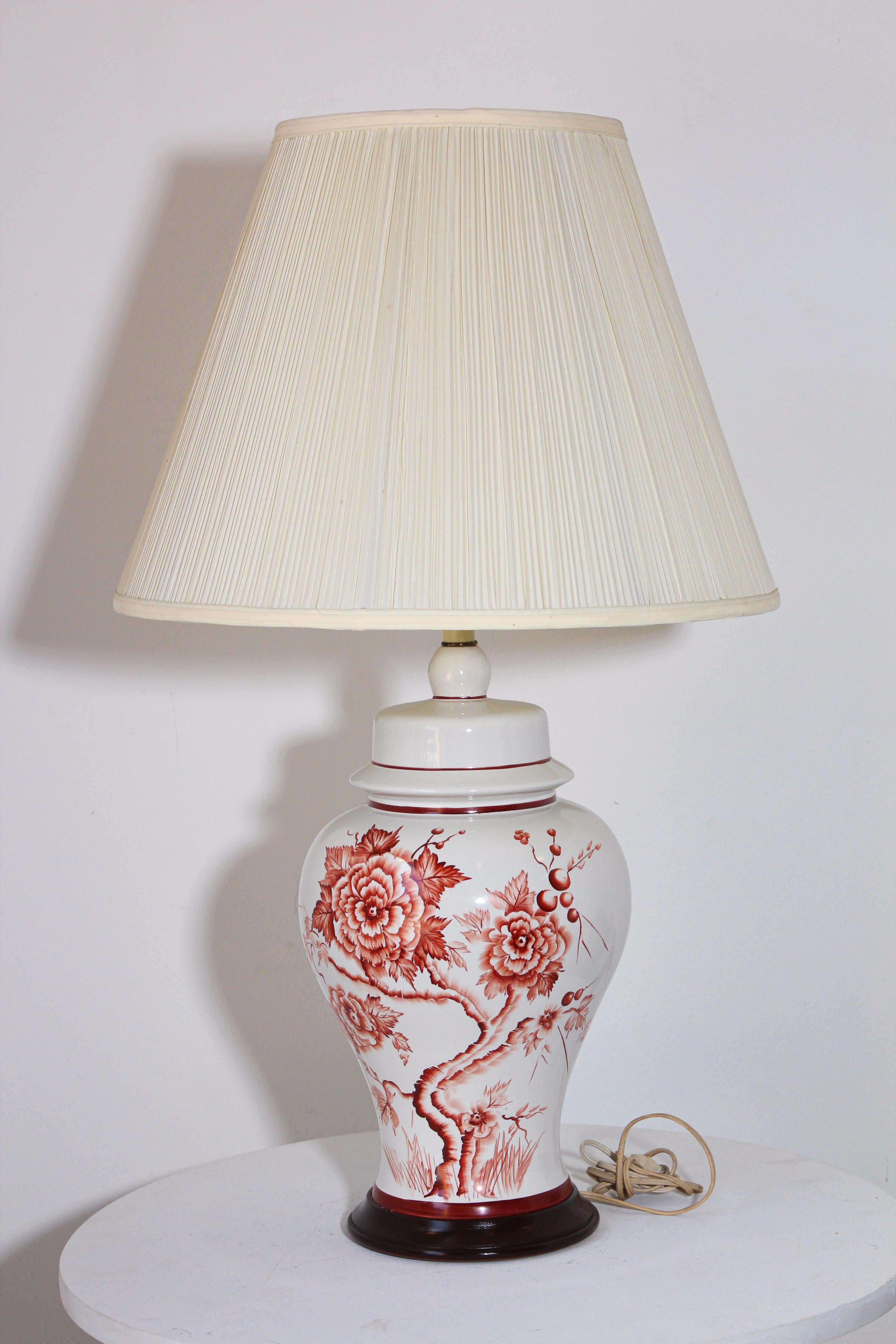 Vintage Chinese table lamp made from a white porcelain urn painted with a floral red roses design around mounted on a brown wooden base and fitted with brass hardware.
Measures: Total height with shade: 32