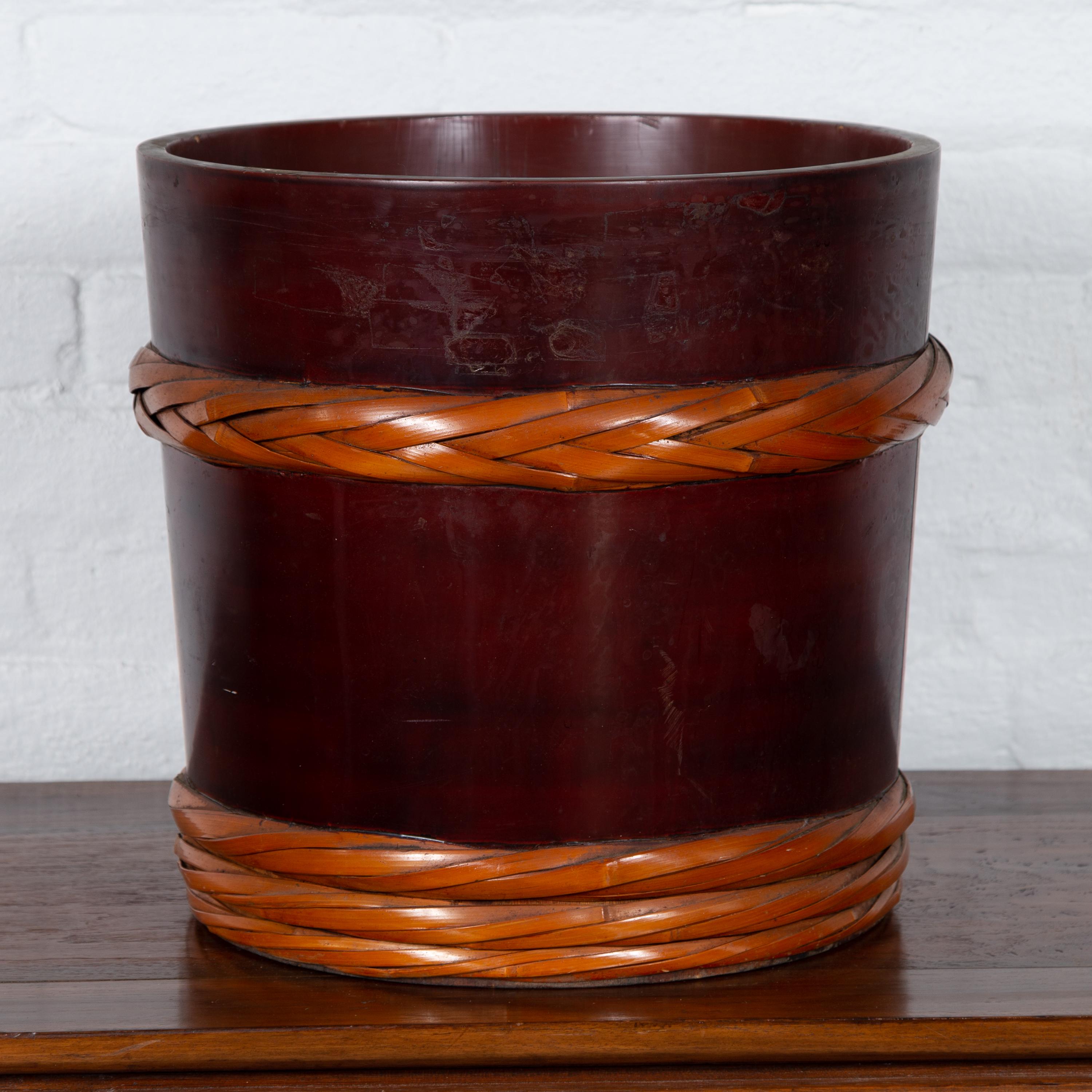 A vintage Chinese barrel planter from the 20th century, with rope design. Born in China, this charming barrel planter is probably between 40 and 80 years old. Presenting a cylindrical wooden body boasting a deep brown color with red undertone, the