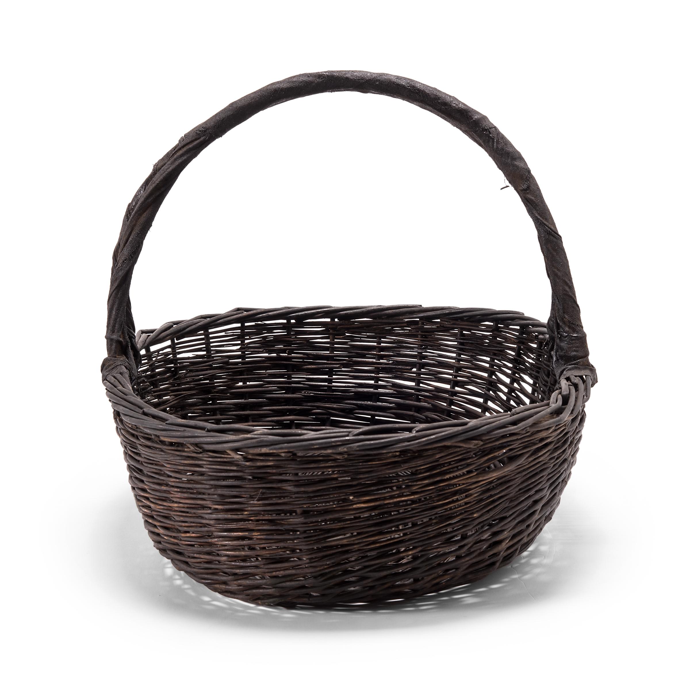 It's easy to imagine the original owner of this basket walking to market on a summer day with the arched handle slung over their arm. Used for carrying food or harvesting vegetables from the garden, this dark, woven basket is a beautiful example of