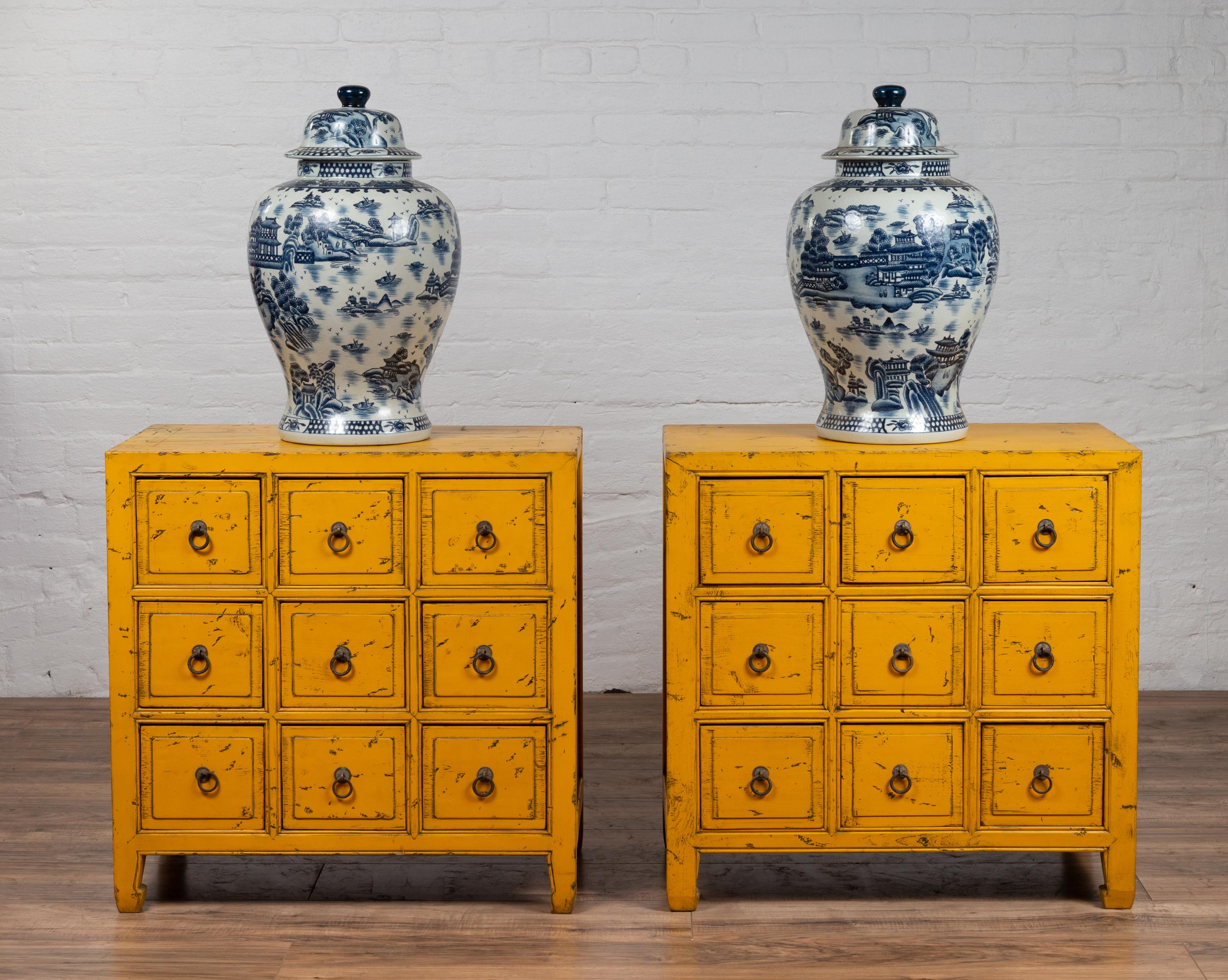 A pair of vintage Chinese yellow painted nine-drawer apothecary bedside chests from the mid-20th century, with distressed finish and black splatter. Born in China during the mid-century period, each of this charming pair of apothecary chests