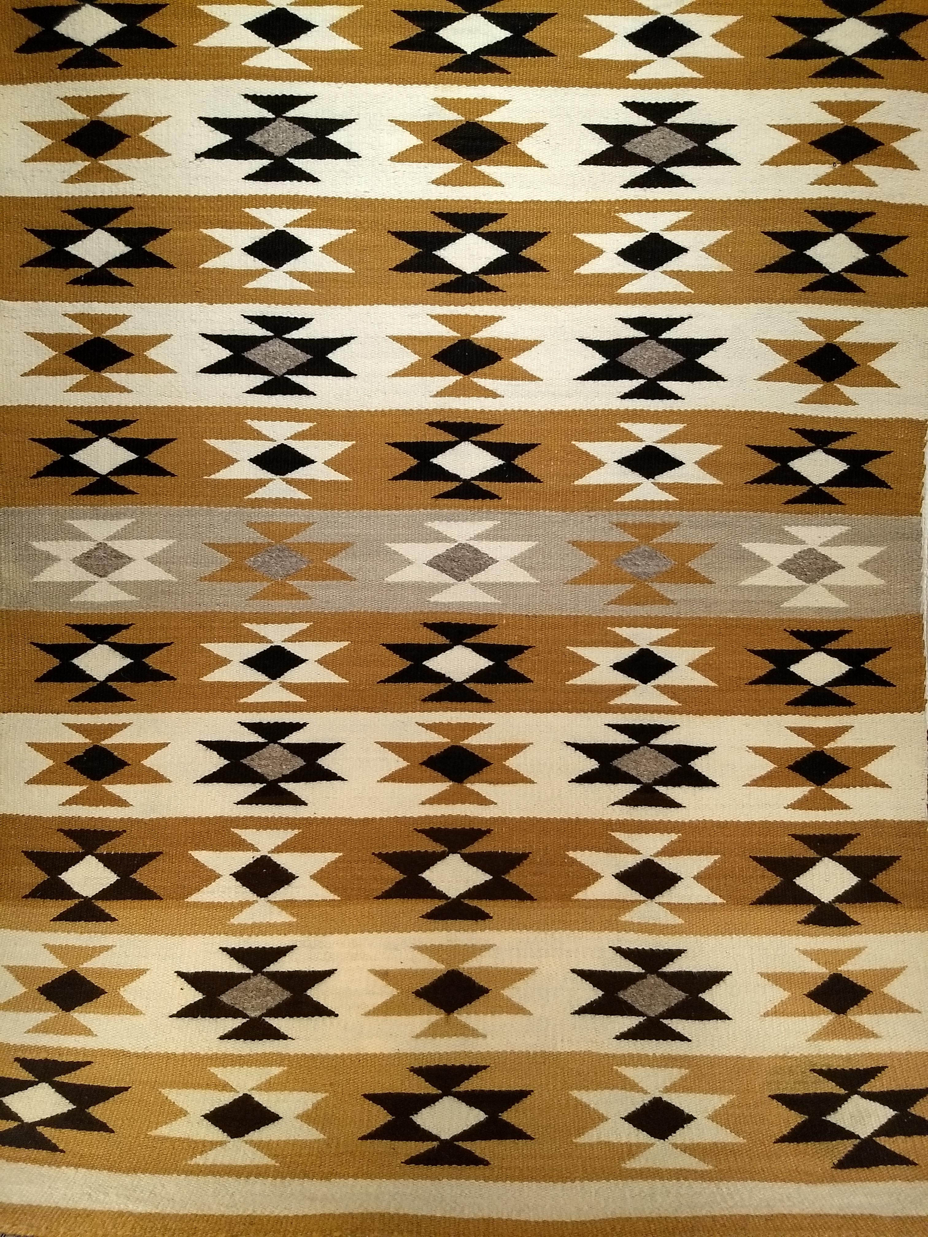 Vintage Native American Navajo Rug in a Chinle revival pattern in earth tone colors including yellow, brown, black, ivory, and gray.  The vintage Navajo rug is woven of native hand-spun wool in a Chinle revival pattern. This style of Navajo Regional