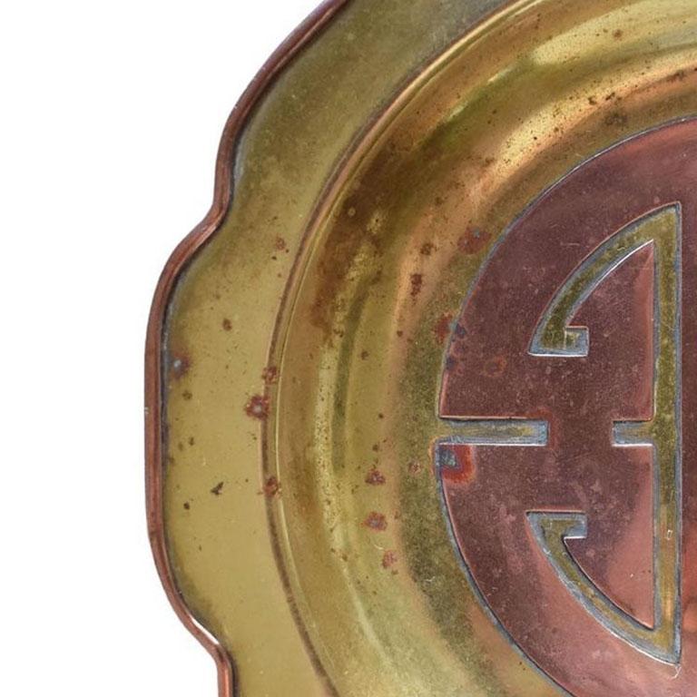 A beautiful chinoiserie catchall, ashtray, or trinket dish. This piece is round with scalloped edges. It is created from brass and decorated with copper accents. The scalloped edges have a copper hue, and the interior of the dish has a copper