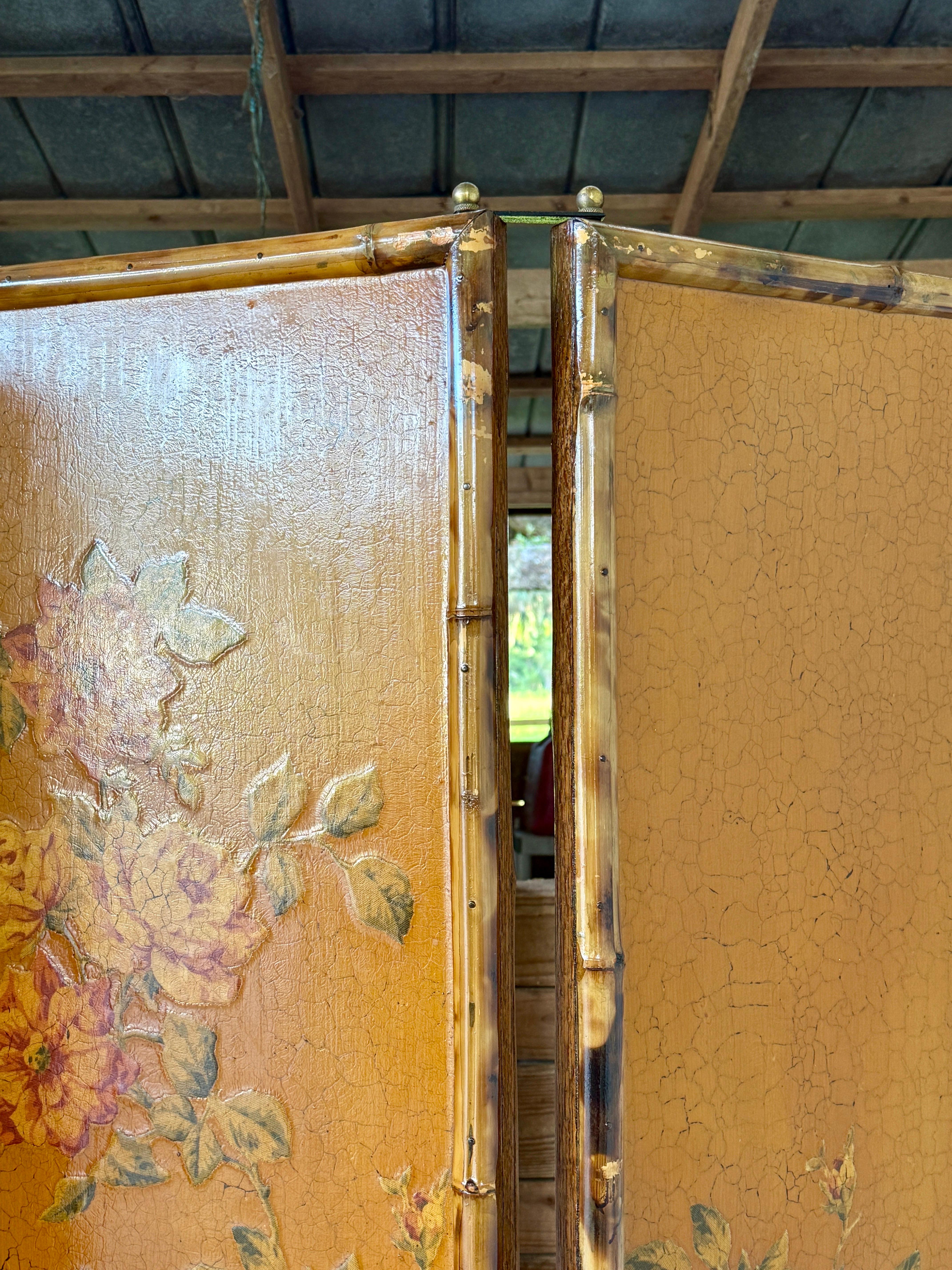 A charming and decorative piece, this vintage three-panel folding screen features a bamboo frame with a beautifully aged lacquered floral chinoiserie design in warm ochre tones. The screen’s surface has a pronounced craquelure effect and visible