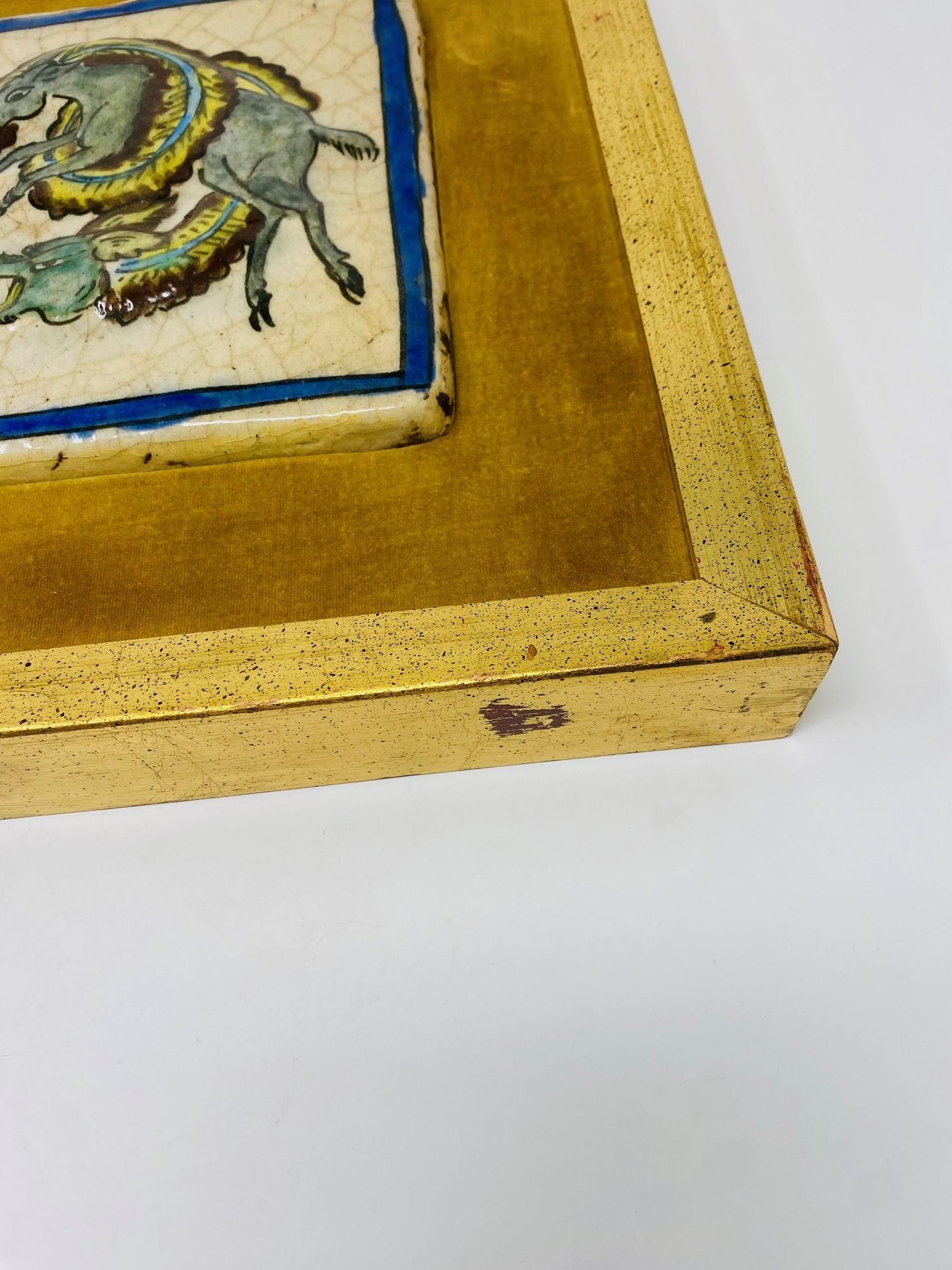 Beautifully framed art piece that evokes style and elegance. This beautiful antique chinoiserie tile is delightfully framed in rich gold velvet and gilt wood. The resulting piece is full of glamour and chic. The antique tile depicts 3 a battle