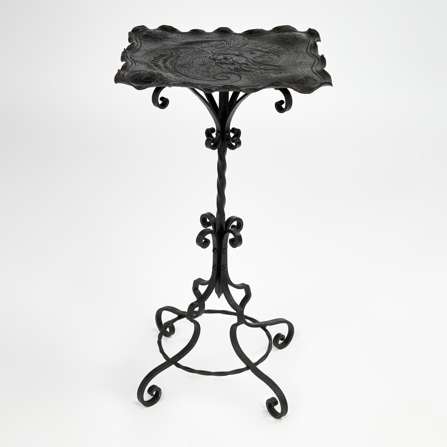 Standout vintage handcrafted iron table or stand having a top with organic form, rolled edges and inscribed dragon on a base with rolled ornaments and four scrolled legs. 