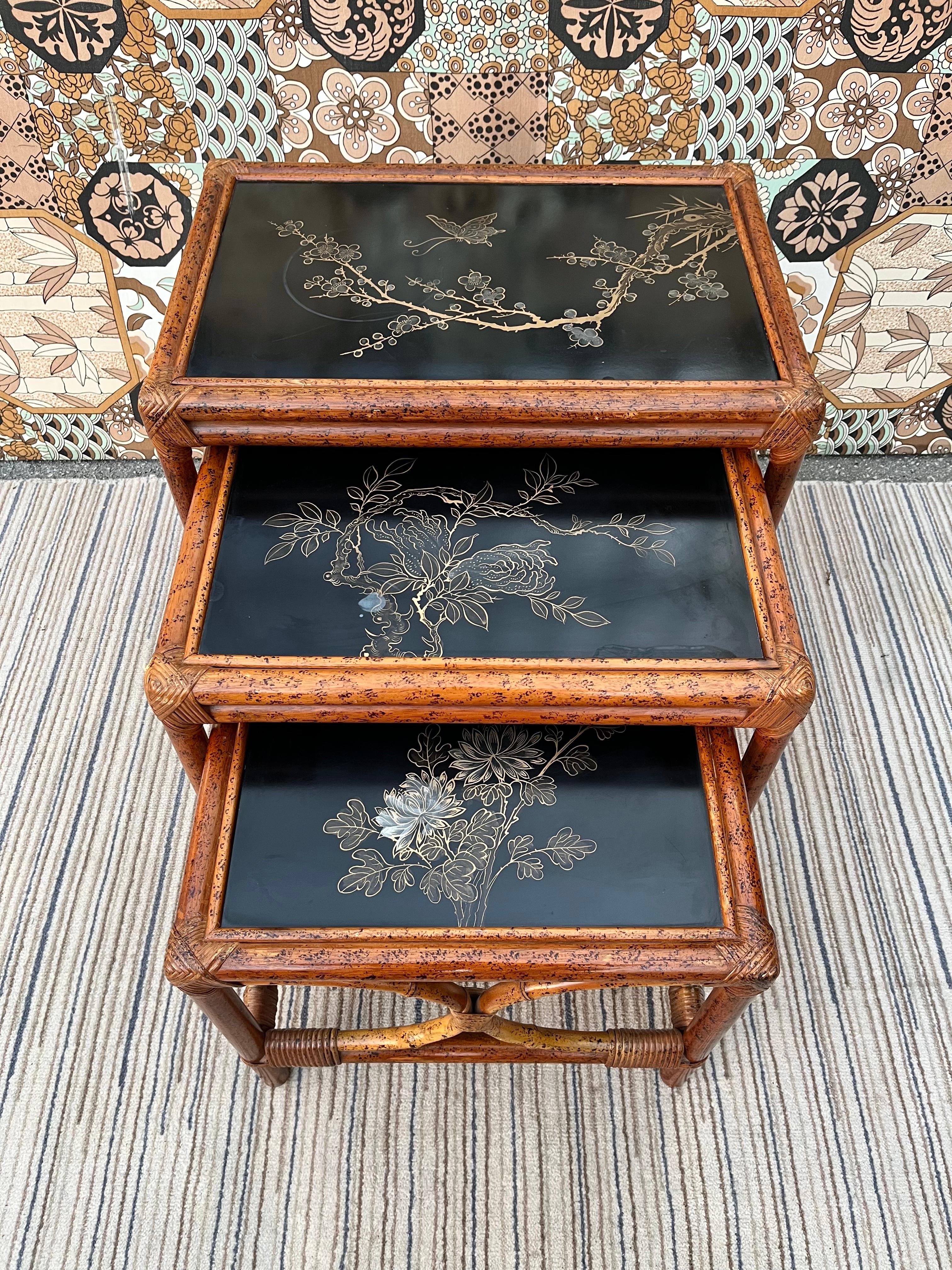 A set of three vintage chinoiserie Rattan nesting tables. circa 1960s.
Feature a tiger bamboo and rattan frame and black laminated top with floral motifs. 
In good original condition with normal signs of wear consistent with age and history. There