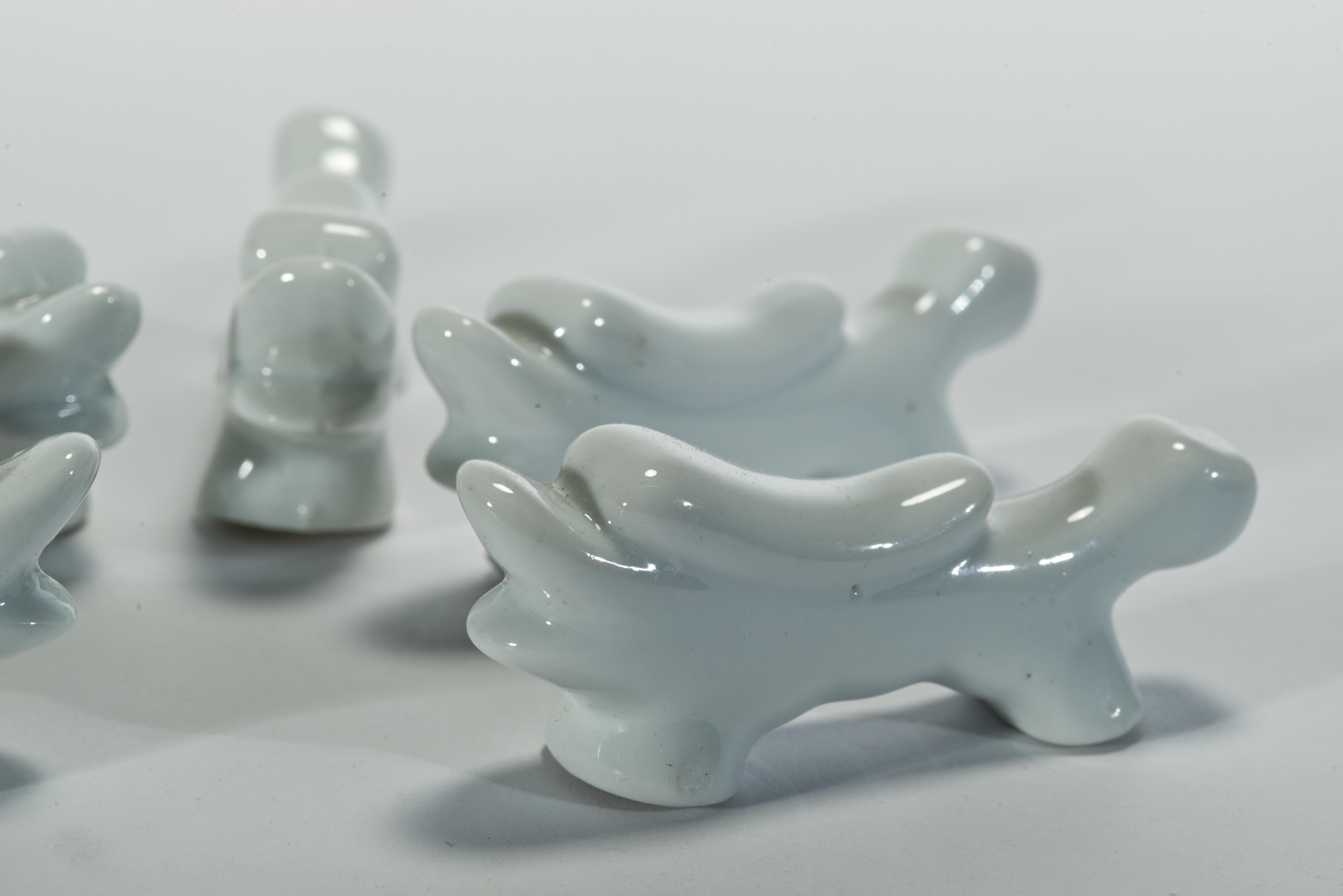 Vintage porcelain knife or chopstick rests feature streamlined abstract dragon shape with short legs and long tail and mane, decorated in monochromatic glossy white glaze. The elongated dragon body forms the knife rest itself; the traditional Blanc