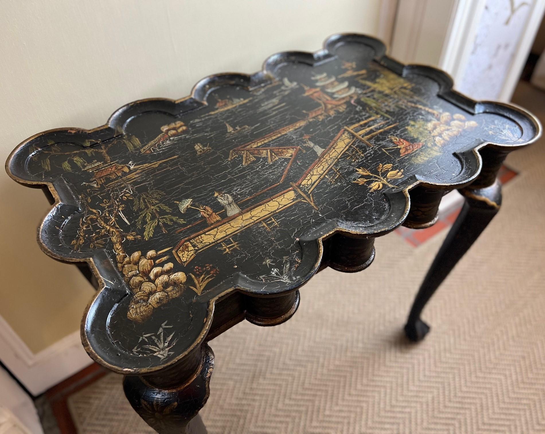Vintage chinoiserie side table featuring a distinctive black crackle paint treatment with gold painted accents, a scalloped top with cabriole legs and ball and claw feet. The top is painted with an extensive chinoiserie style scene detailing boats,