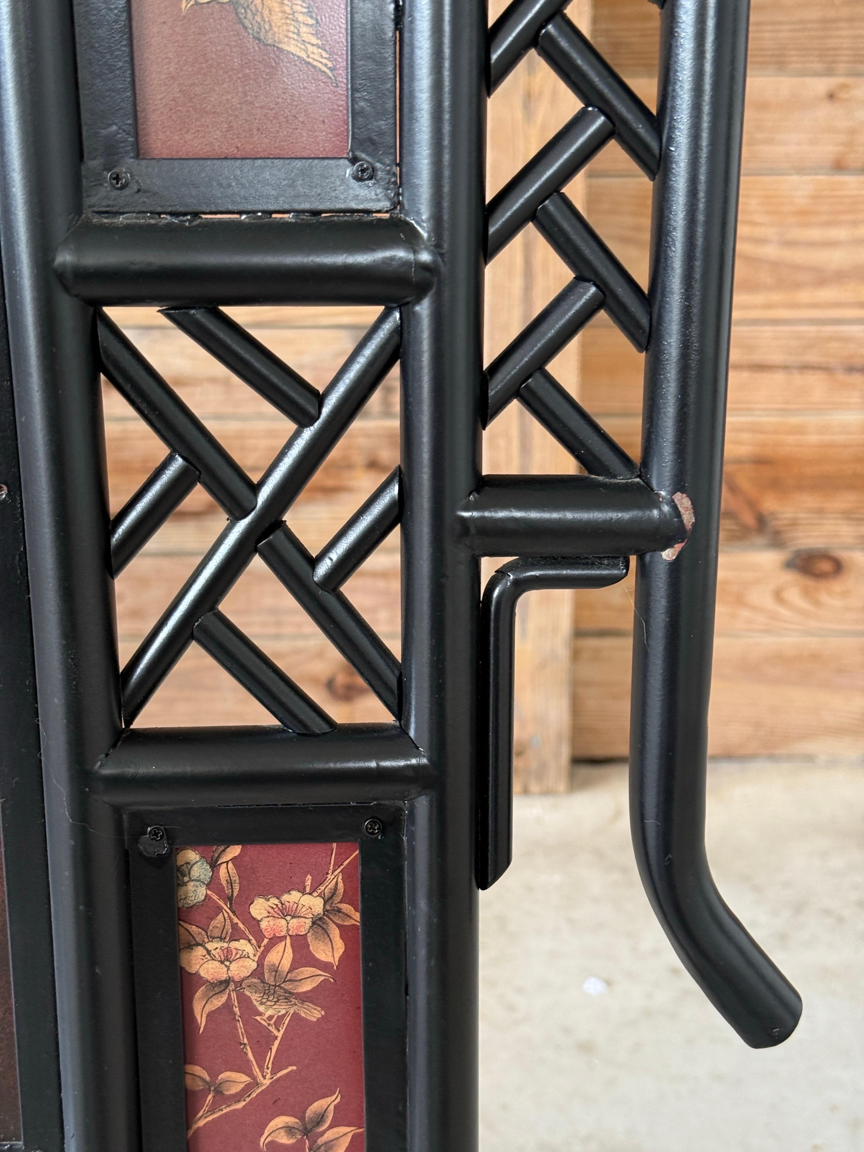 Ein auffälliger Kaminschirm im Vintage-Chinoiserie-Stil aus schwarz lackiertem Metall mit offenen Laubsägearbeiten und von Pagoden inspirierten Linien. In der Mitte sind zwei goldene Kraniche inmitten von Glyzinienkaskaden zu sehen, umgeben von