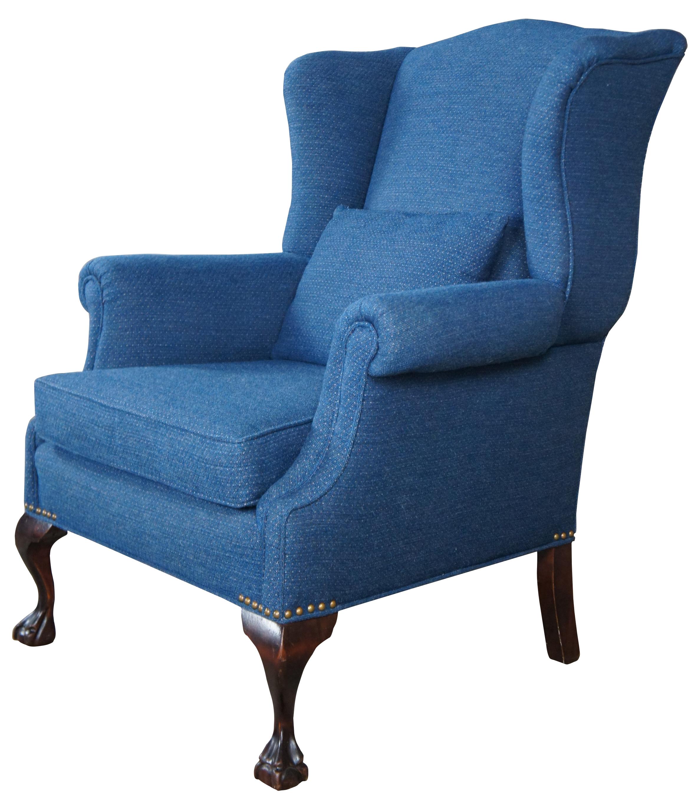 A traditional wingback, circa mid 20th century. Made from mahogany with ball and claw feet. Features a blue upholstery with rolled arms, flared back, bolster pillow and nail head trim.
 