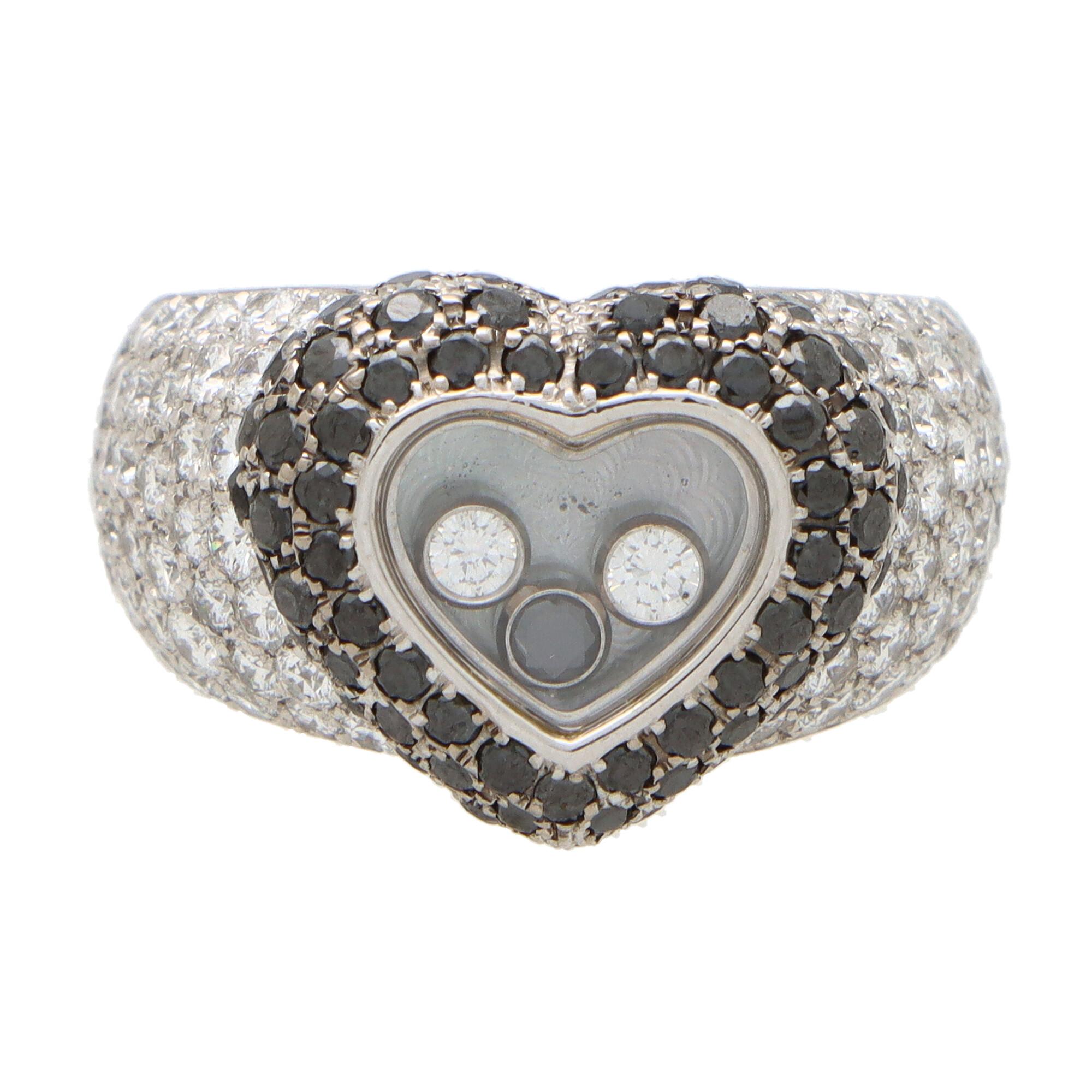 A unique vintage Chopard black and white diamond ‘Happy Diamonds’ ring set in 18k white gold. 

The ring depicts an open-heart motif with three floating rub-over set diamonds to centre. The diamonds float in a crystal topped casing and the heart is