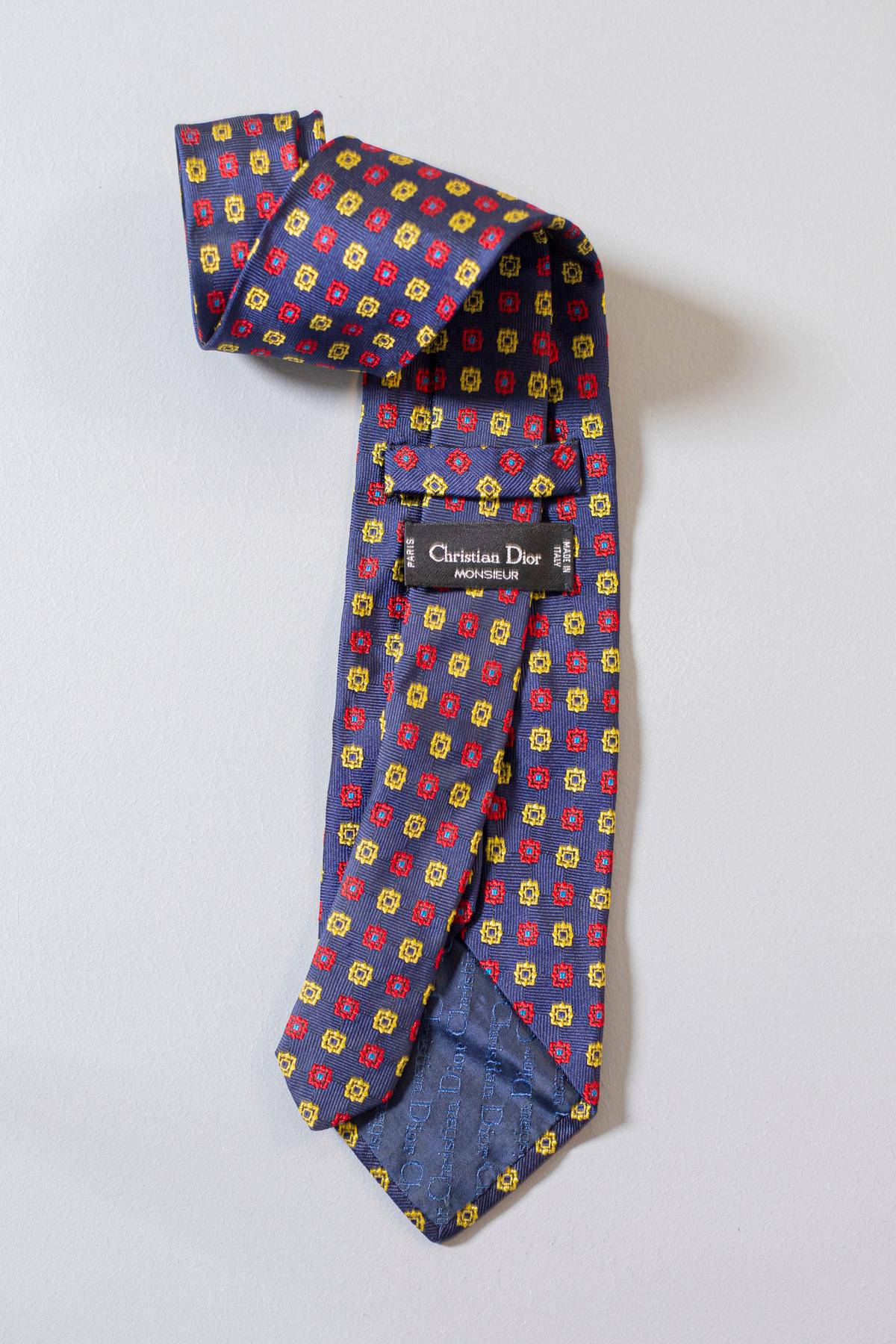 Designed by Christian Dior for his Monsieur Collection, this vintage tie is made in all-silk. It is decorated with red and yellow motifs on a dark blue background. This tie is perfect for a formal night out or for a work event.