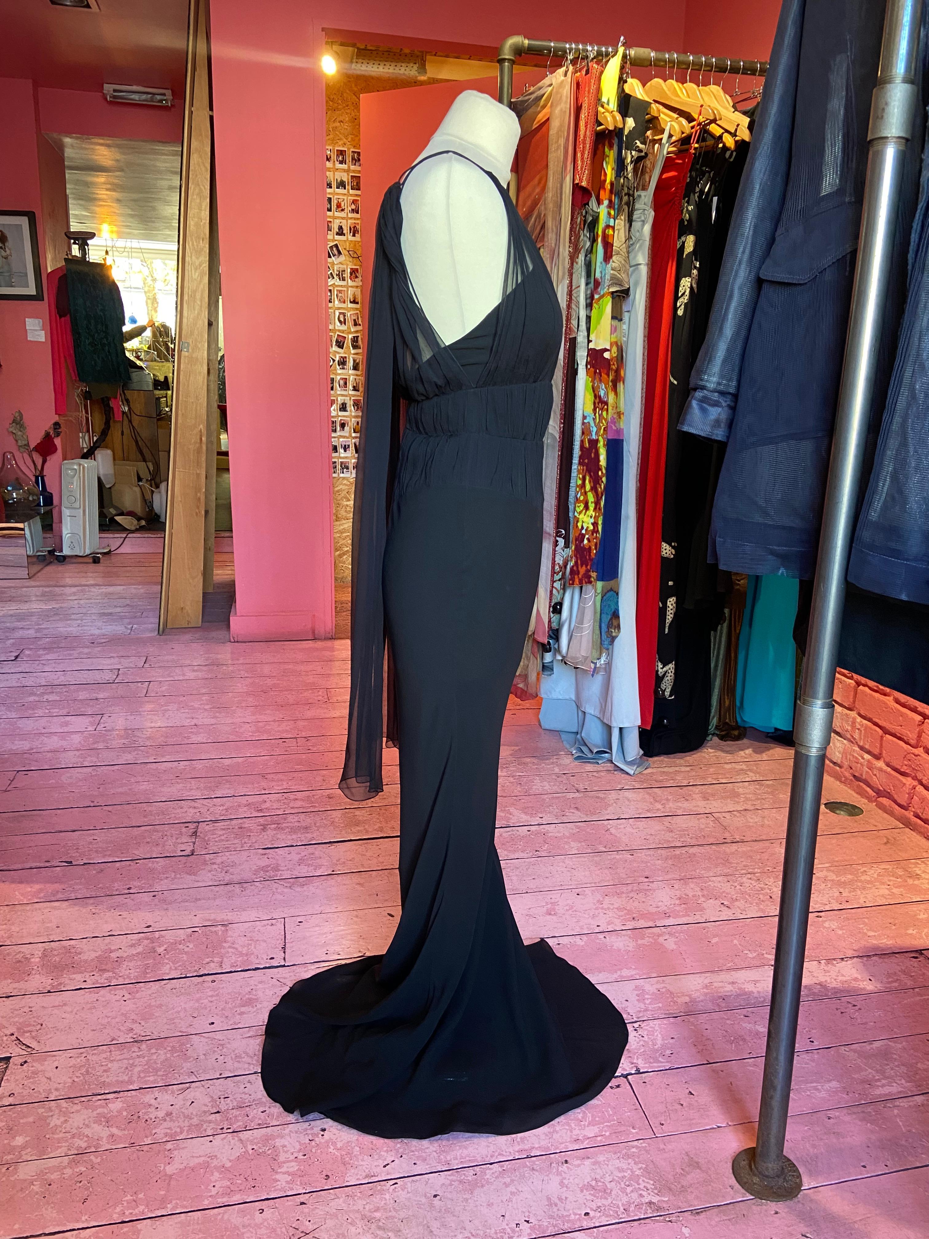 We are excited to present this Vintage Christian Dior by John Galliano S/S 2006 Silk Chiffon Dress. Features a black silk chiffon with a ruched bodice and attached scarf detail at the shoulders. fastens with silk covered buttons. In excellent