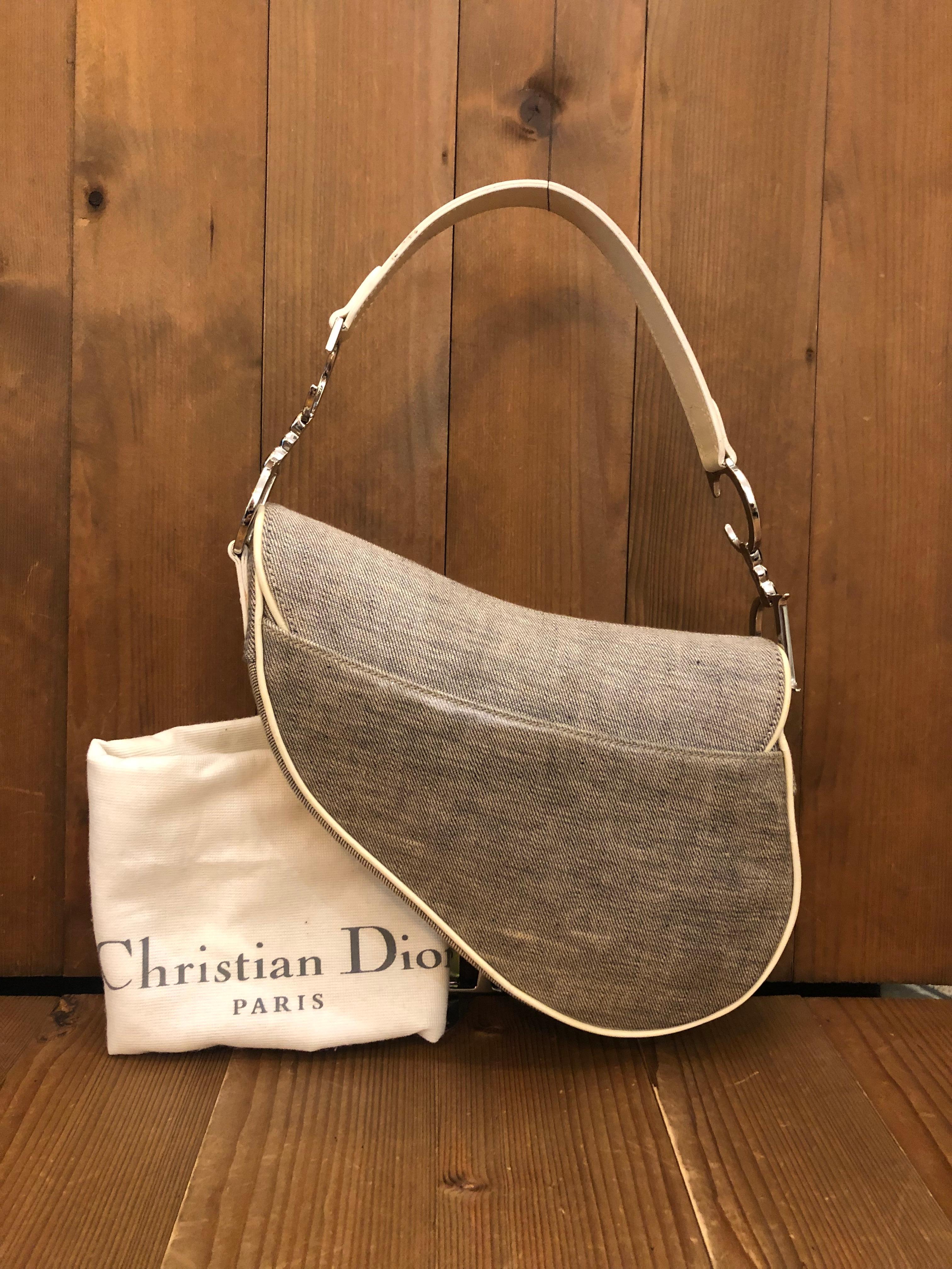This iconic Christian Dior Saddle Bag is crafted of canvas and laminated canvas in gray featuring silver toned hardware. Front flap Velcro closure opens to a beige fabric interior featuring a zippered pocket. The back also features a patch pocket
