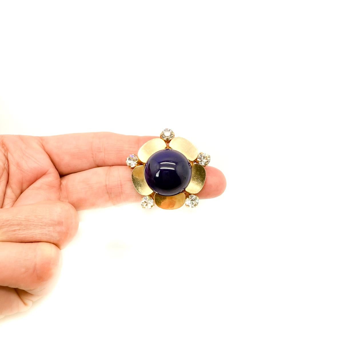 Découvrez l'élégance intemporelle avec cette exquise broche Fleur de Lapis Vintage Dior de 1967. Véritable trésor de l'ère flower power, cette broche Dior rare présente des pétales stylisés en ton or, ornés de chatons en cristal sertis de griffes,