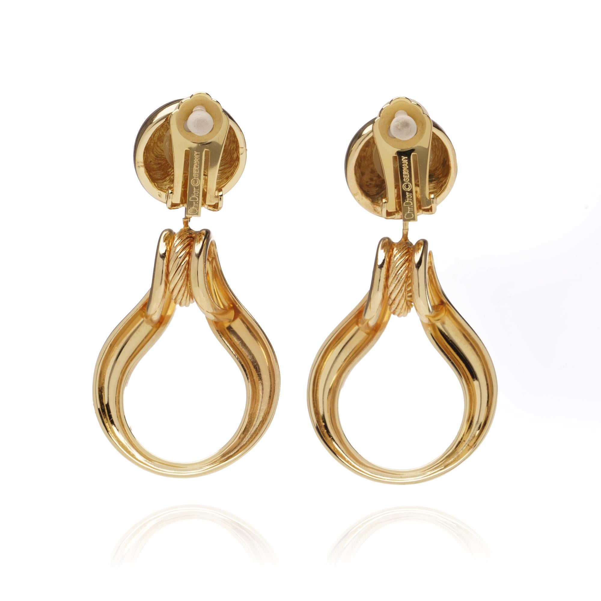A pair of striking vintage Christian Dior statement earrings, designed in a bold sculptural form. Crafted in polished gold-tone metal, the earrings feature a smooth domed stud top with an elegant open teardrop-shaped drop, suspended with a twisted
